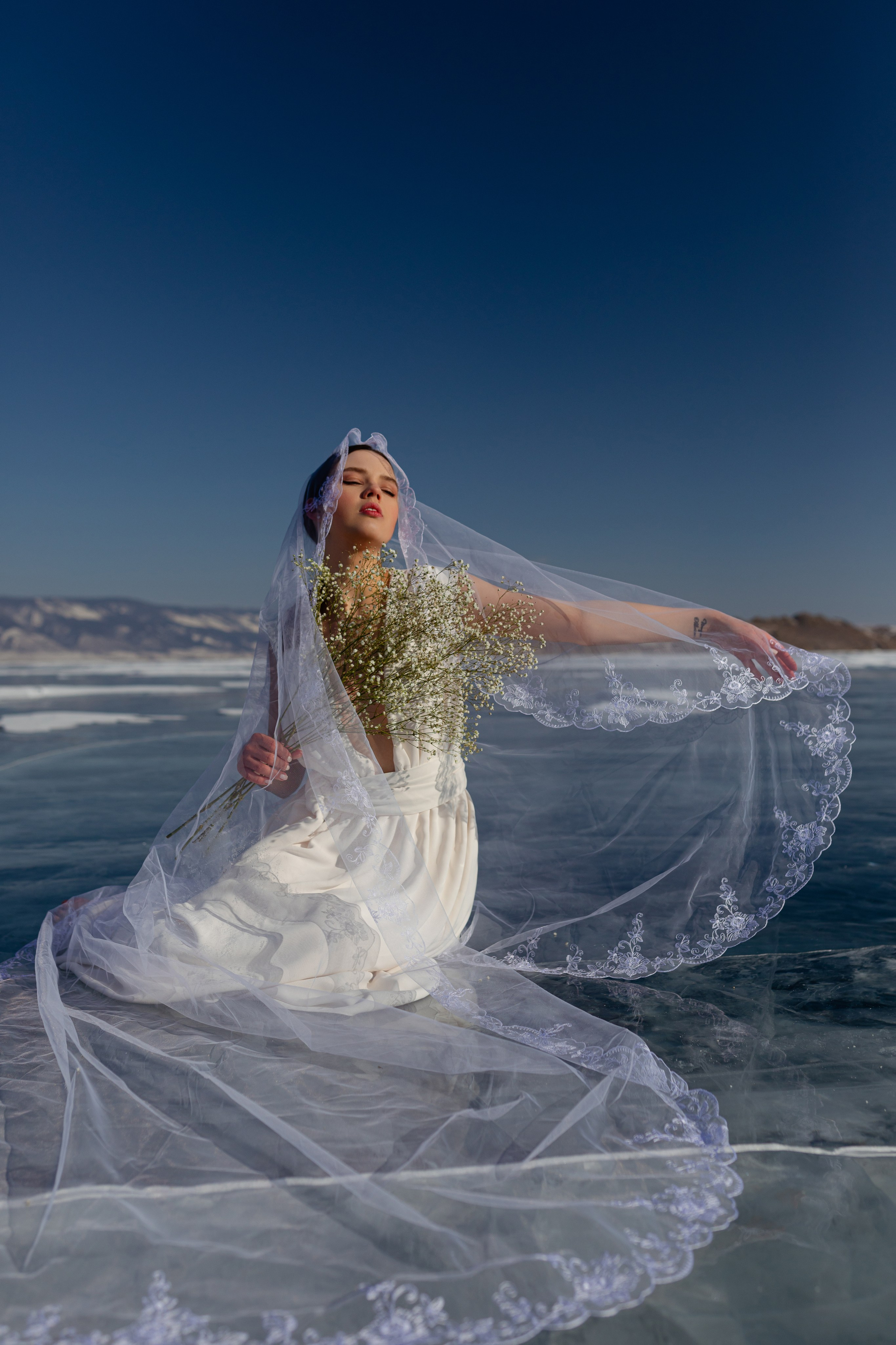 Красивая девушка в белом платье из фатой на замёрзшем озере Байкал