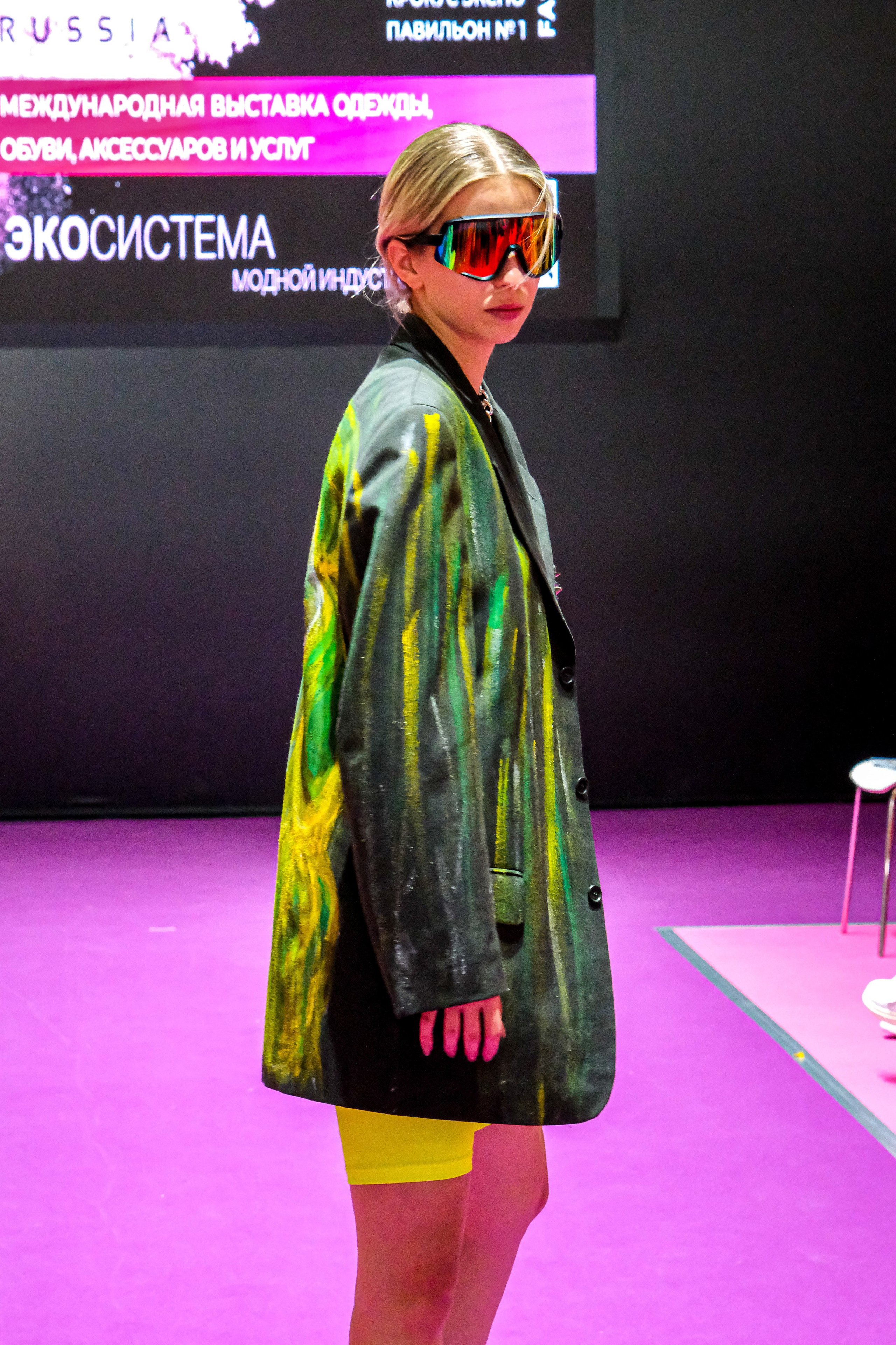  "Модели в ярких нарядах проходят по подиуму во время показа мод, освещенные яркими софитами и окруженные восторженными зрителями."