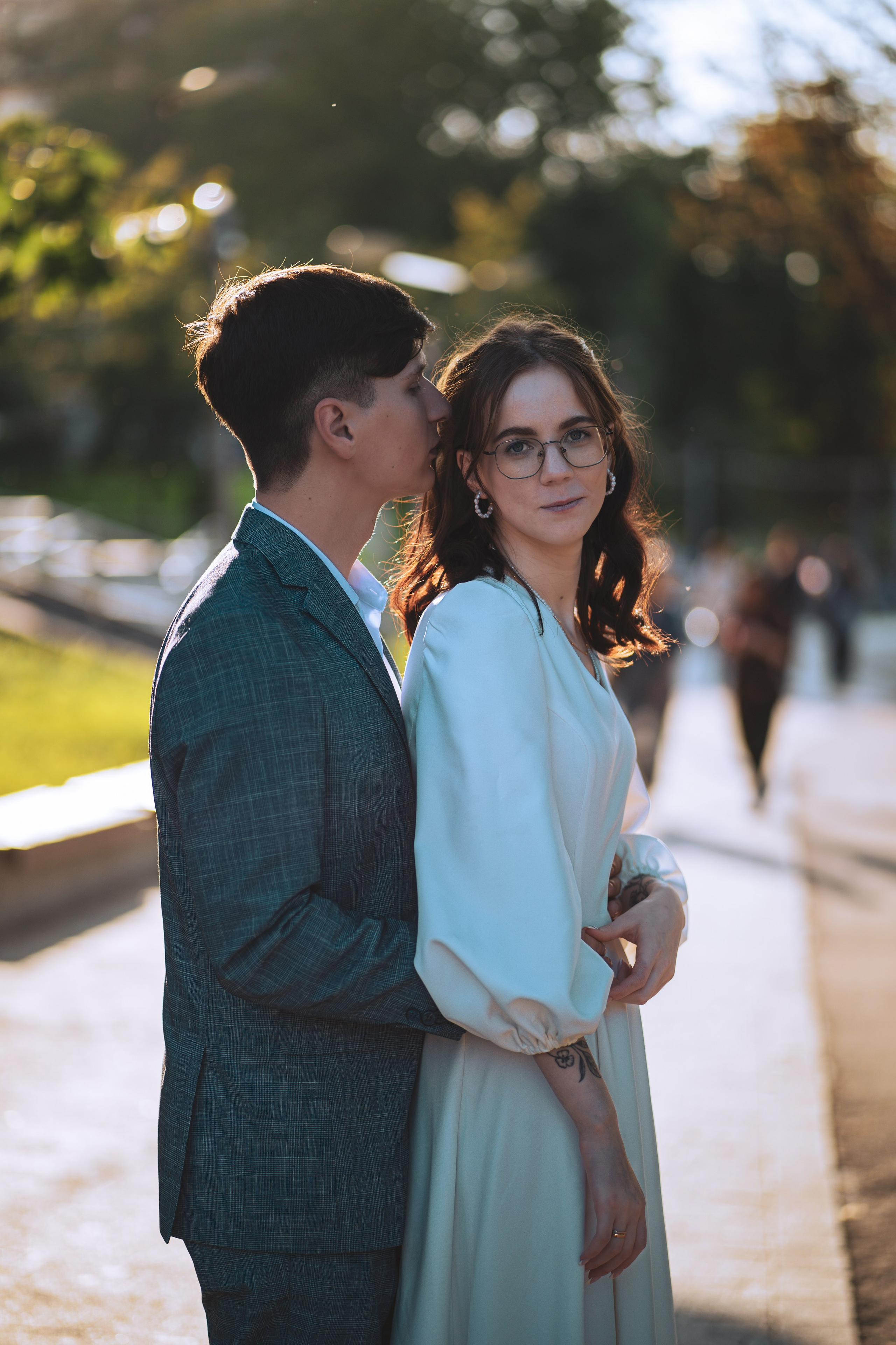 Жених обнимает свою любимую со спины в парке