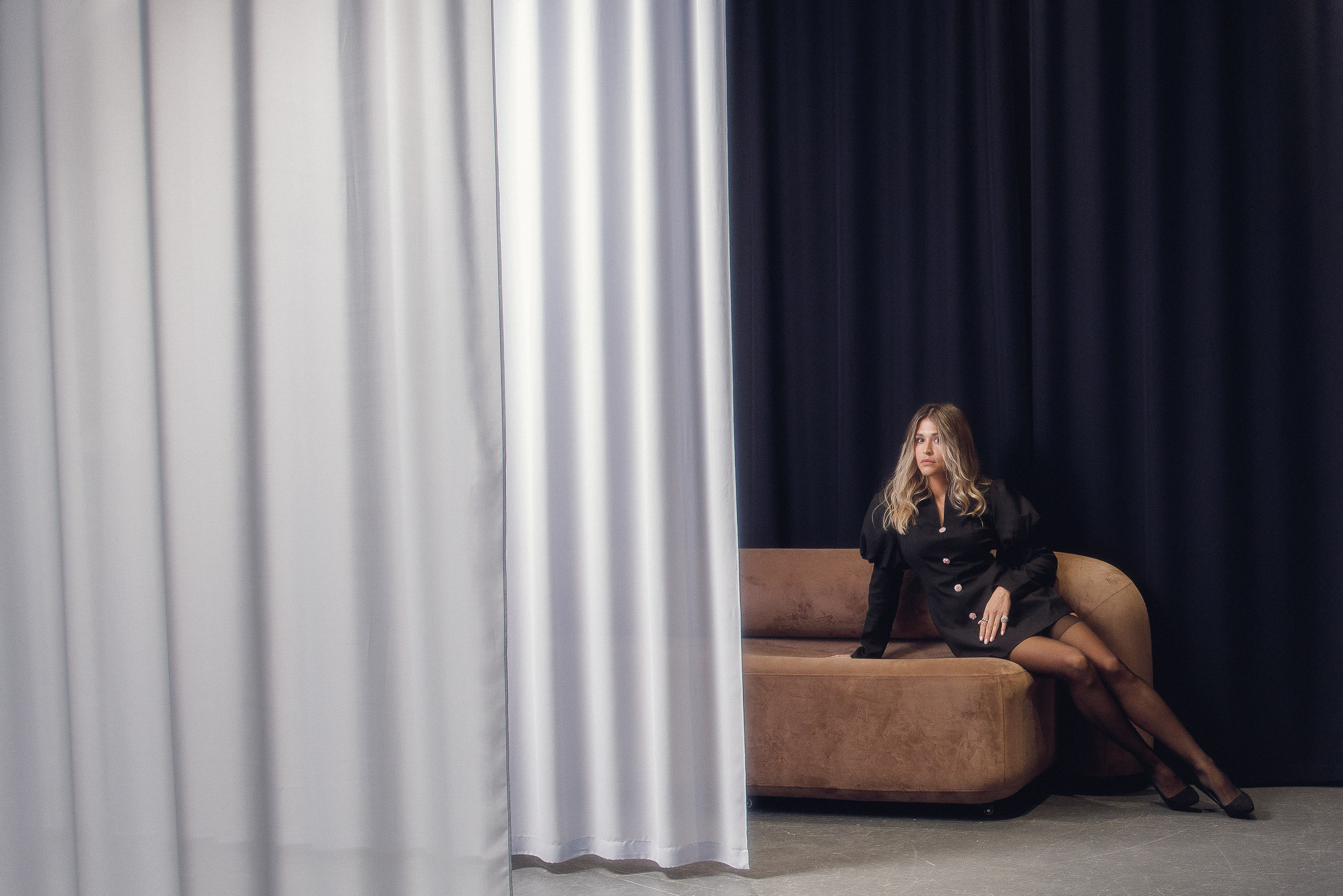 Портрет девушки в черном платье-жакете на диване, студийная съемка.