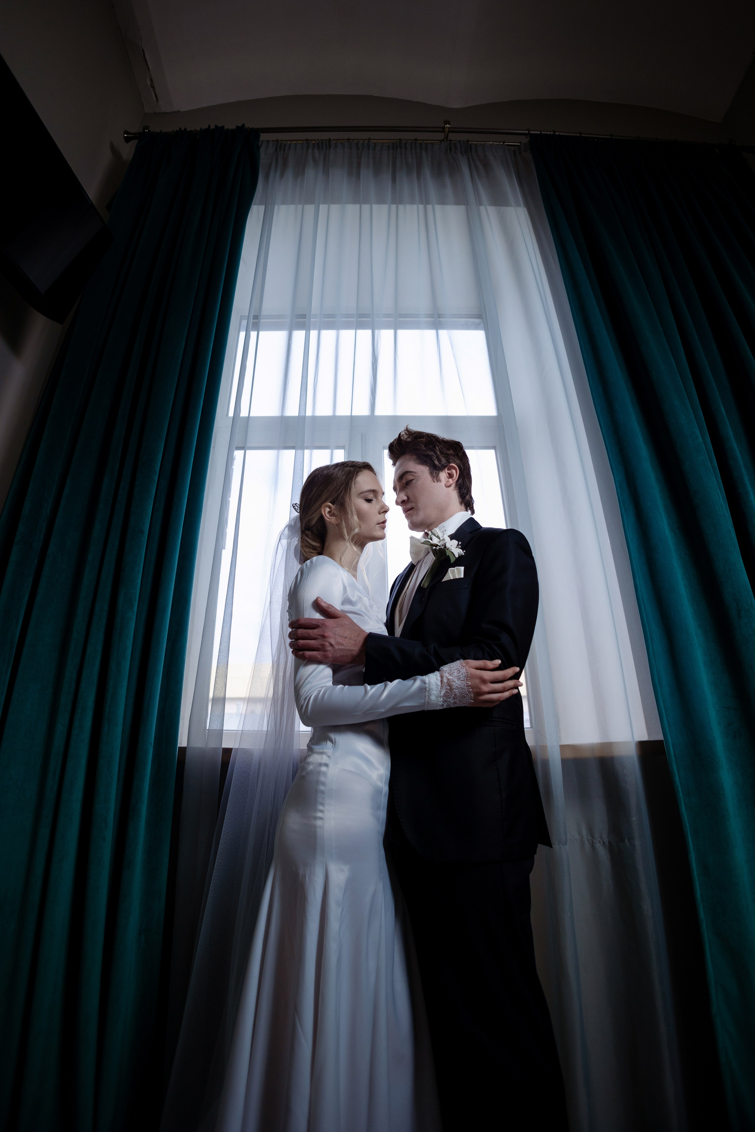 Жених и невеста смотрят друг на друга с любовью на фоне окна.