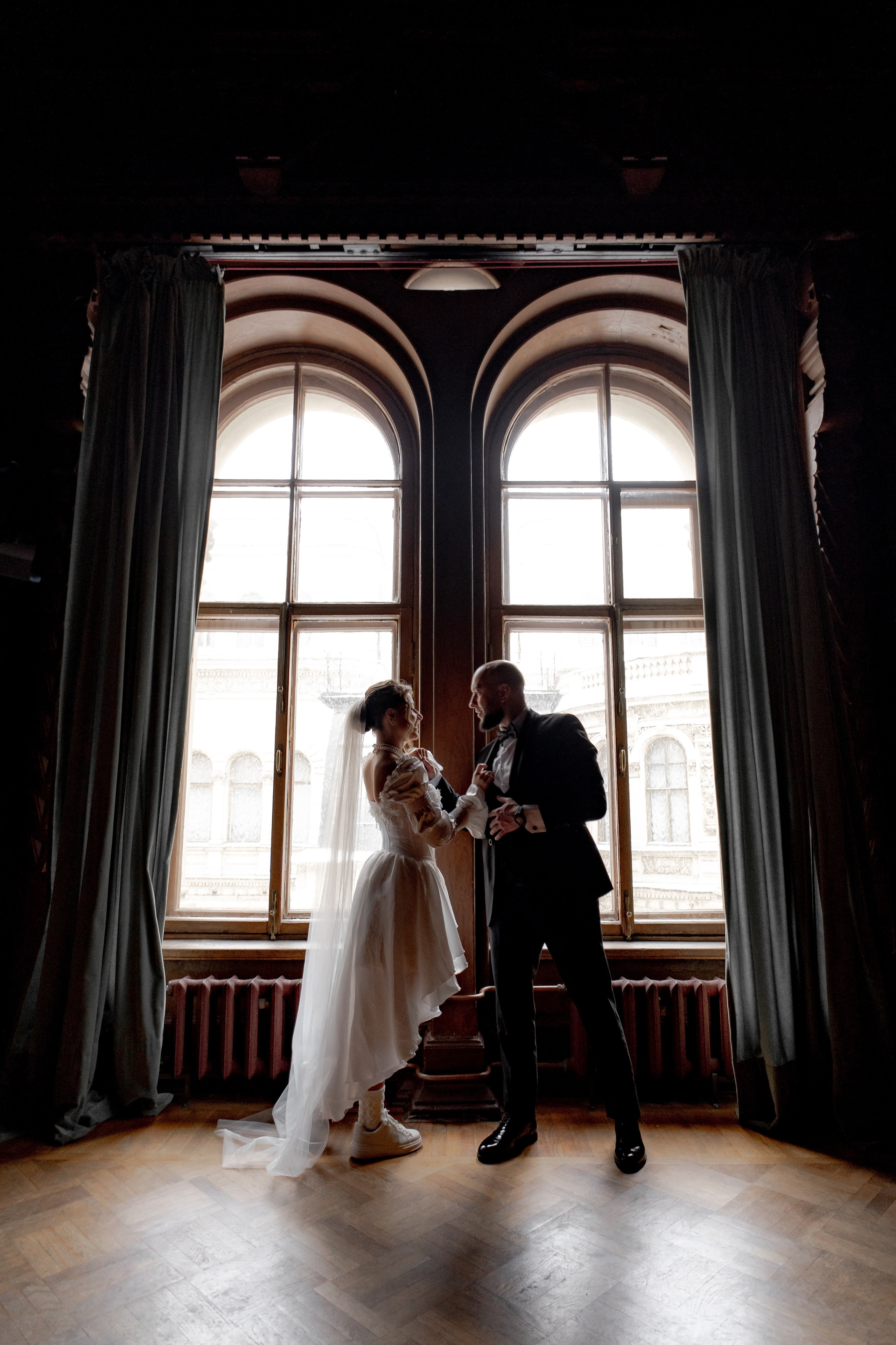 жених и невеста стоят у окна в контровом свете в доме учёных в Дубовом зале