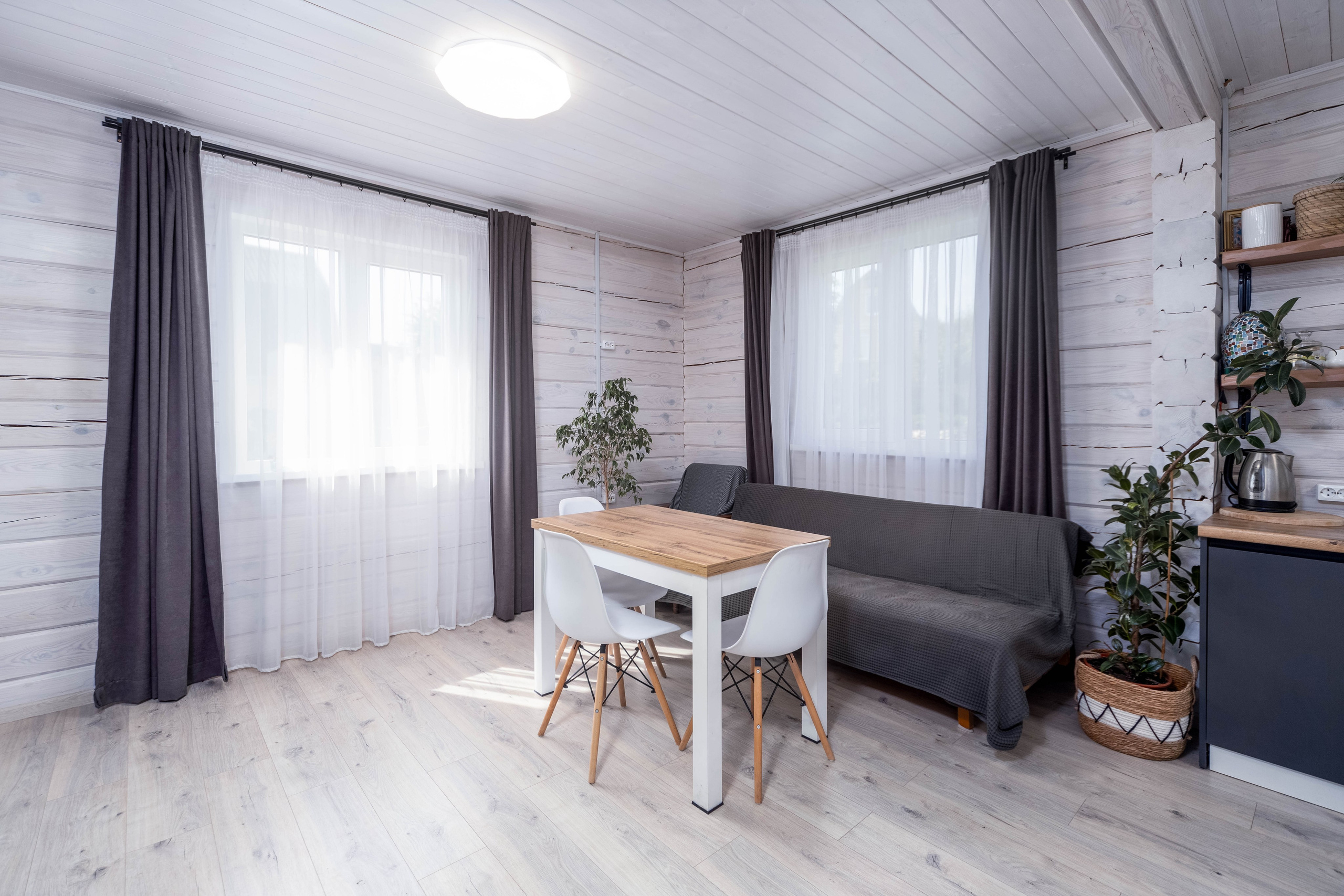 Обеденный стол, два больших окна во двор и диван в кухне-гостиной большого дома под Минском