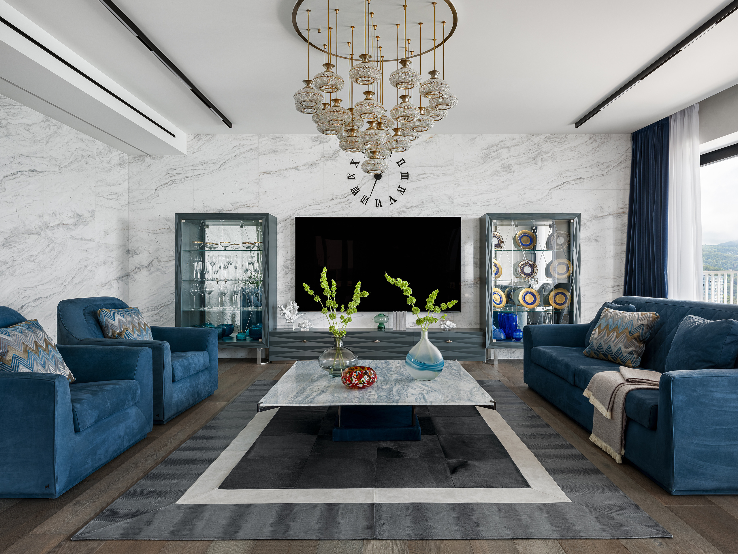 Просторная гостиная в современном стиле с мраморными стенами, панорамным телевизором, синими креслами и дизайнерской люстрой; интерьер оформлен Екатериной Ракитиной, фотосъёмка Сергея Денисенко.
