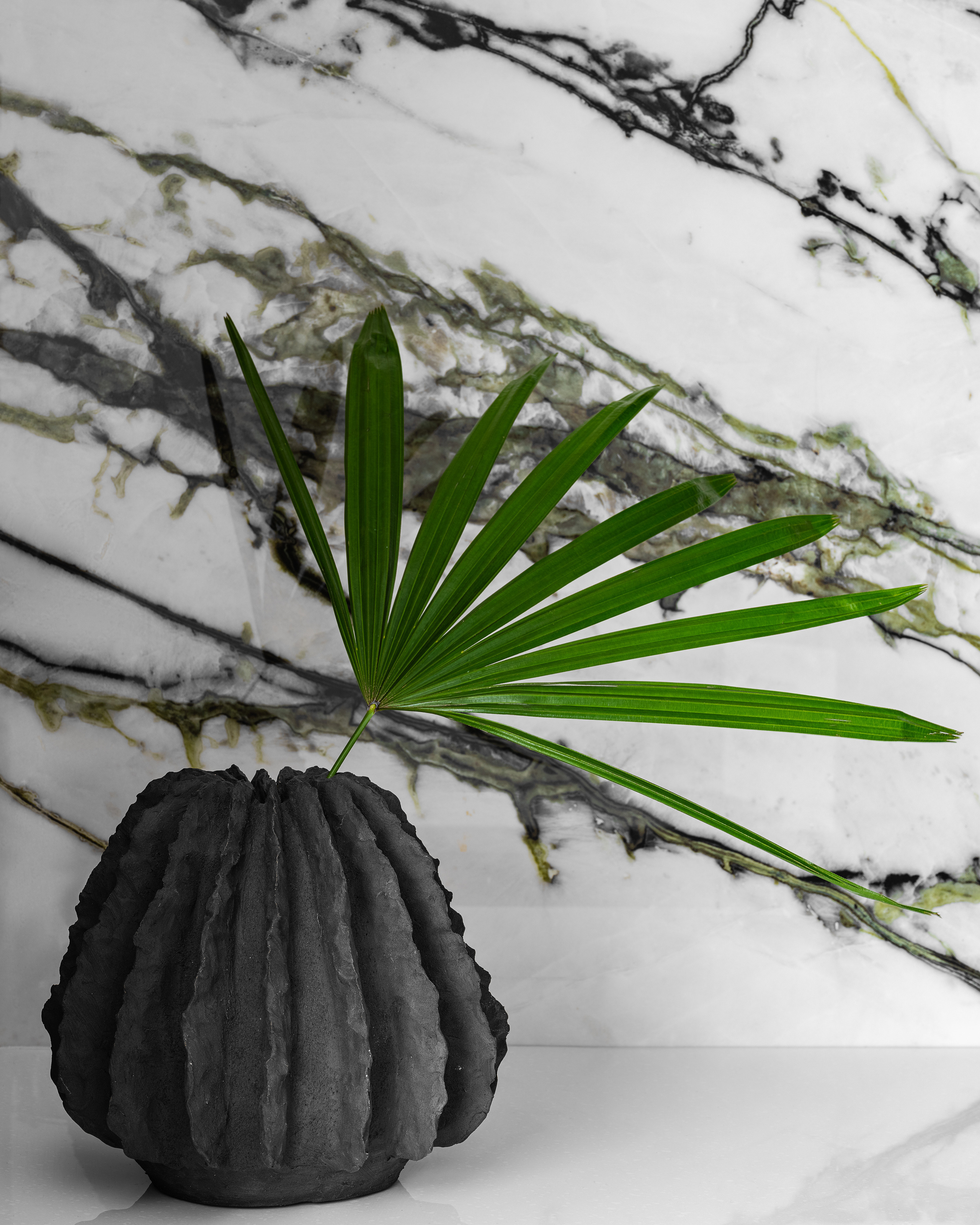 Декор интерьера с дизайнерской вазой в форме кактуса и зелёным пальмовым листом на фоне мраморной стены с черными и зелёными прожилками, стильное решение от Алёны Сверловой, фотография Сергея Денисенко