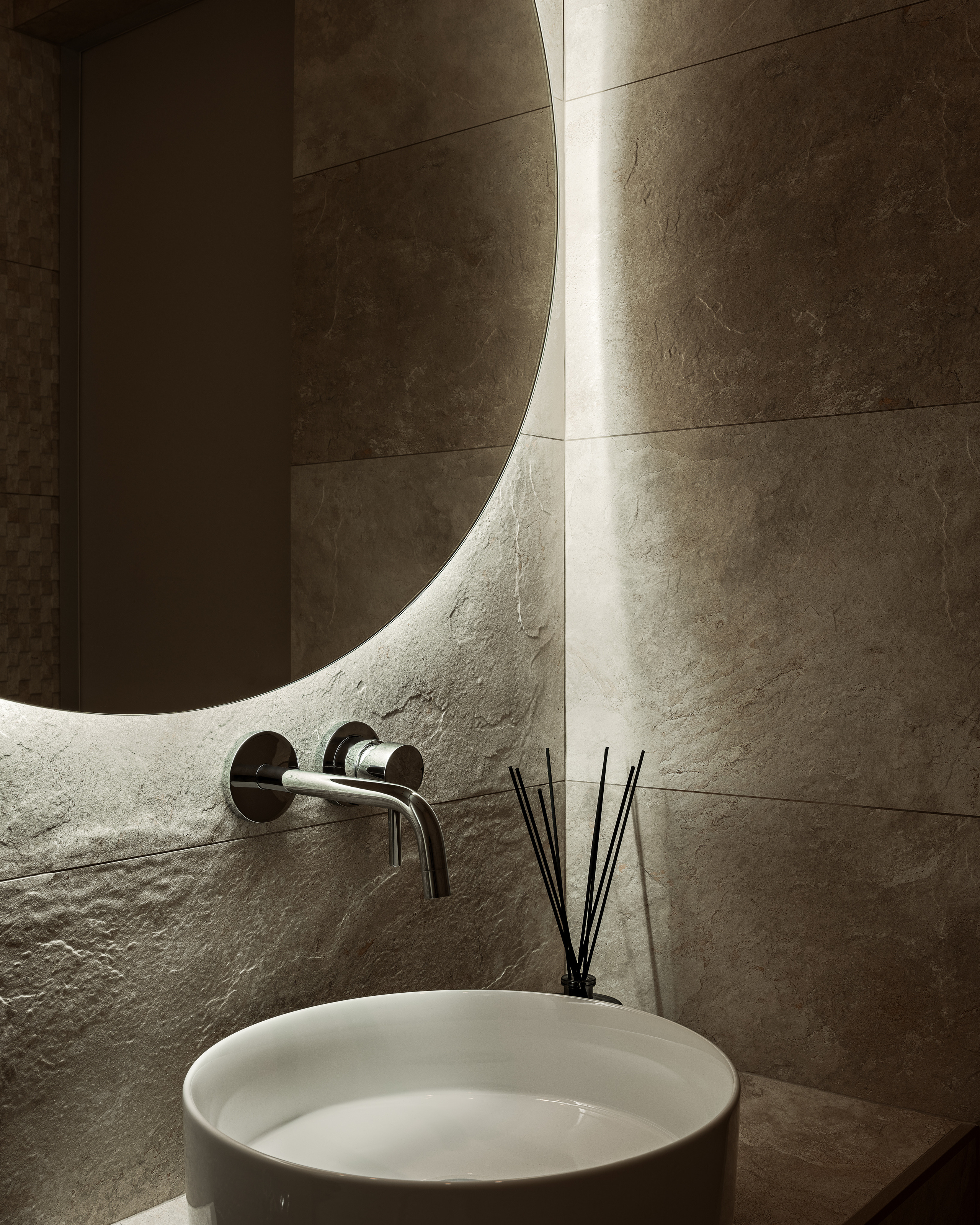 Современный дизайн ванной комнаты с круглым зеркалом с подсветкой, накладной раковиной и встроенным смесителем на фоне каменной плитки, интерьер от дизайнера Алёны Сверловой, фотограф Сергей Денисенко