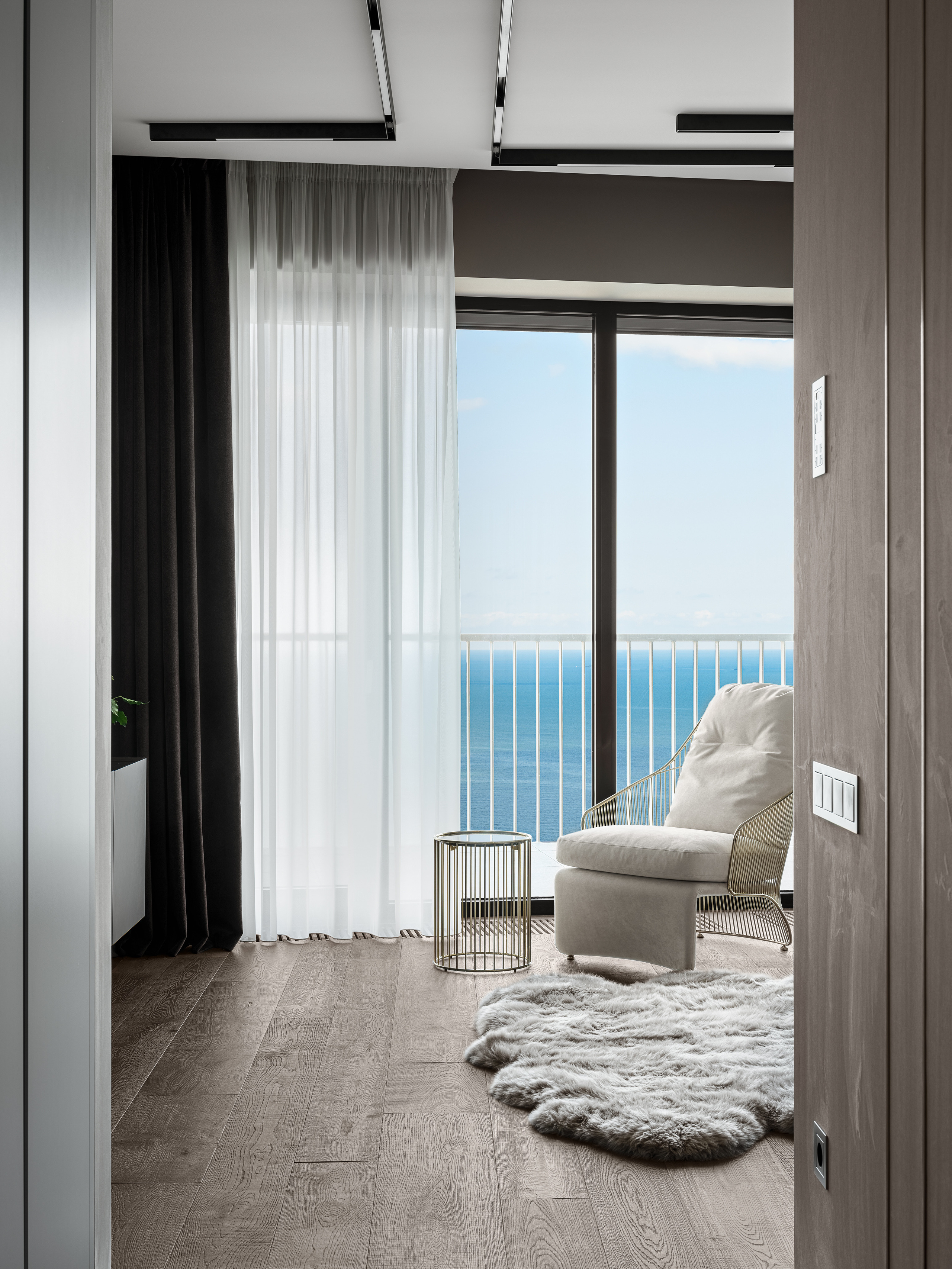 Современный интерьер спальни с панорамным видом на море, акцент на пушистый ковер, мягкое кресло и легкие шторы, минимализм в деталях, авторская работа стилиста Екатерины Ракитиной и фотографа Сергея Денисенко.