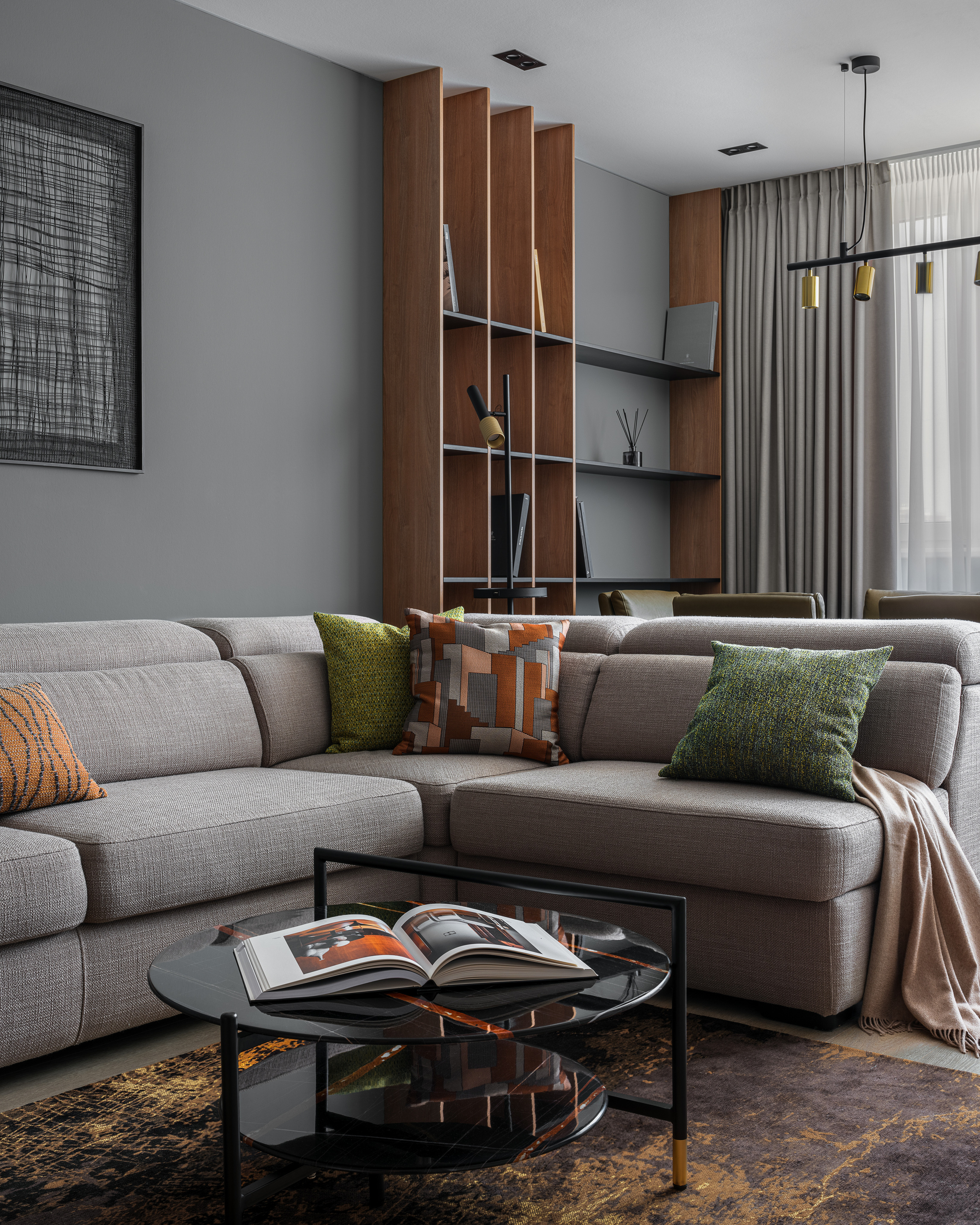 Стильная гостиная с модульным серым диваном, контрастными подушками, журнальным столиком и современным ковром в тёплых оттенках. Деревянный стеллаж добавляет уют. Автор проекта дизайнер Алёна Сверлова, фотограф Сергей Денисенко.