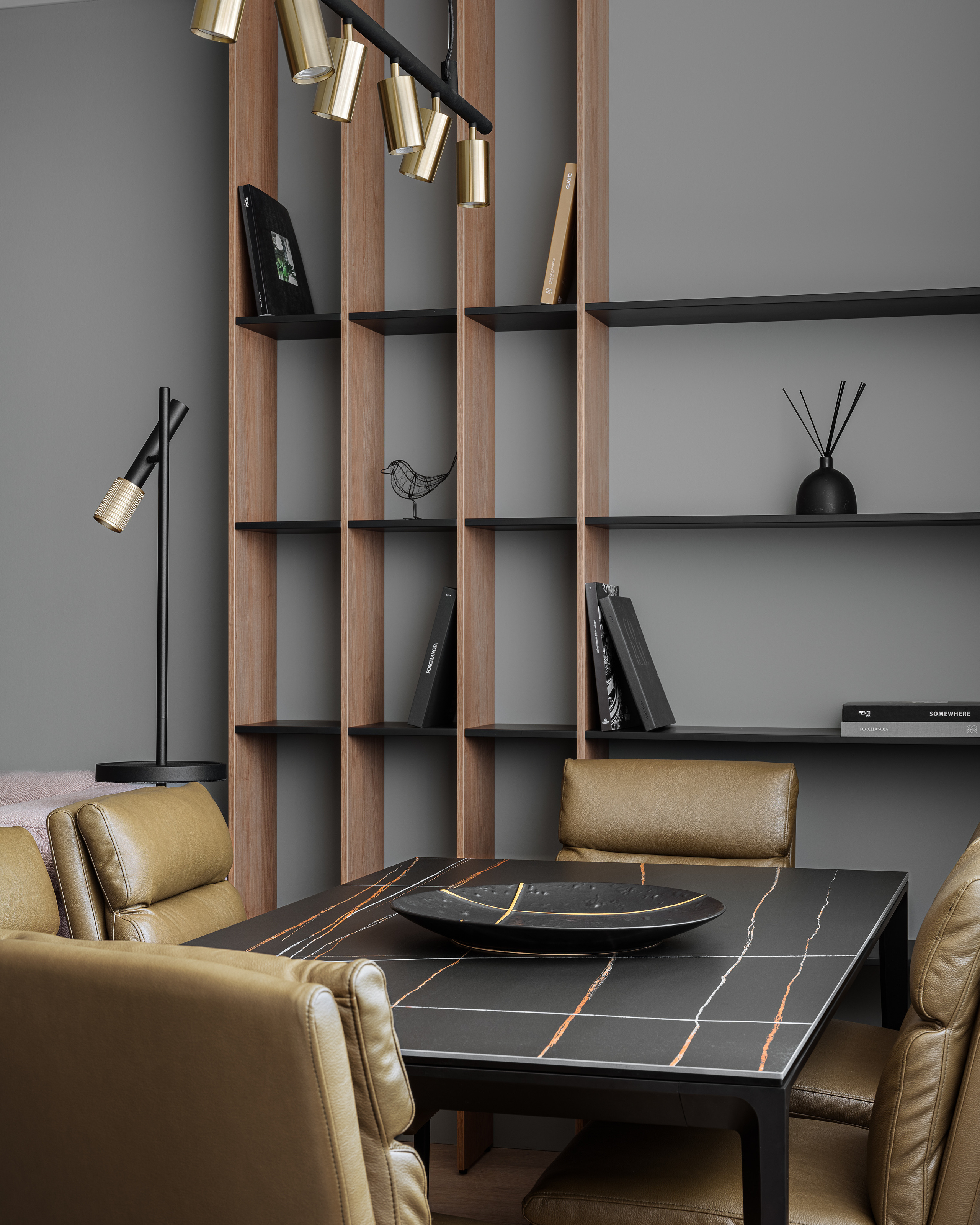 Обеденная зона с черным столом с мраморным узором, мягкими стульями в оливковой коже и высоким стеллажом из дерева с минималистичным декором. Современный интерьер от дизайнера Алёны Сверловой, фотограф Сергей Денисенко.