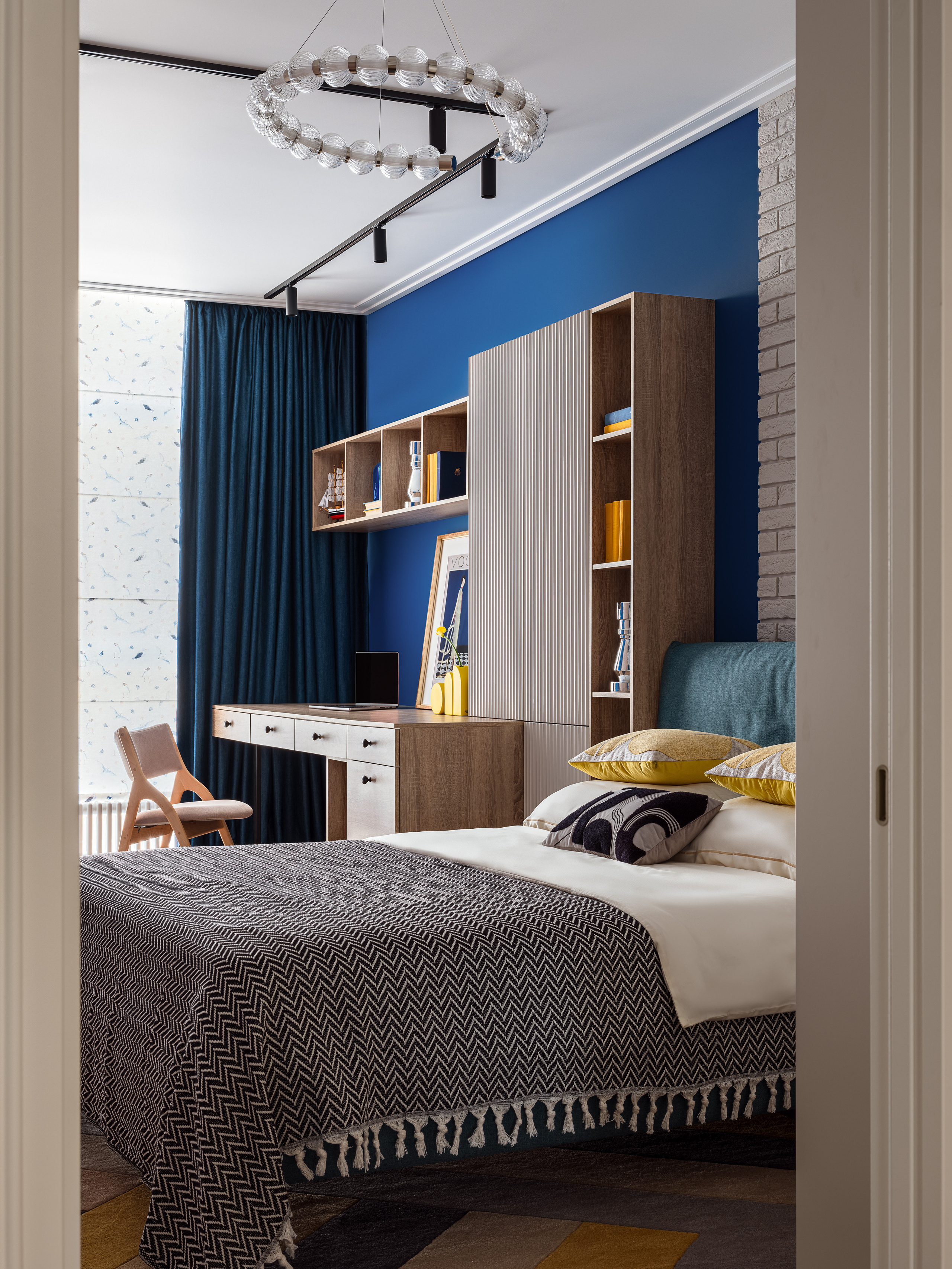 Современная спальня с акцентной синей стеной, рабочей зоной с деревянным столом и яркими желтыми деталями декора. Интерьер от дизайнера Оксаны Магомедовой, стилиста Натальи Якушевой, фото Сергея Денисенко.