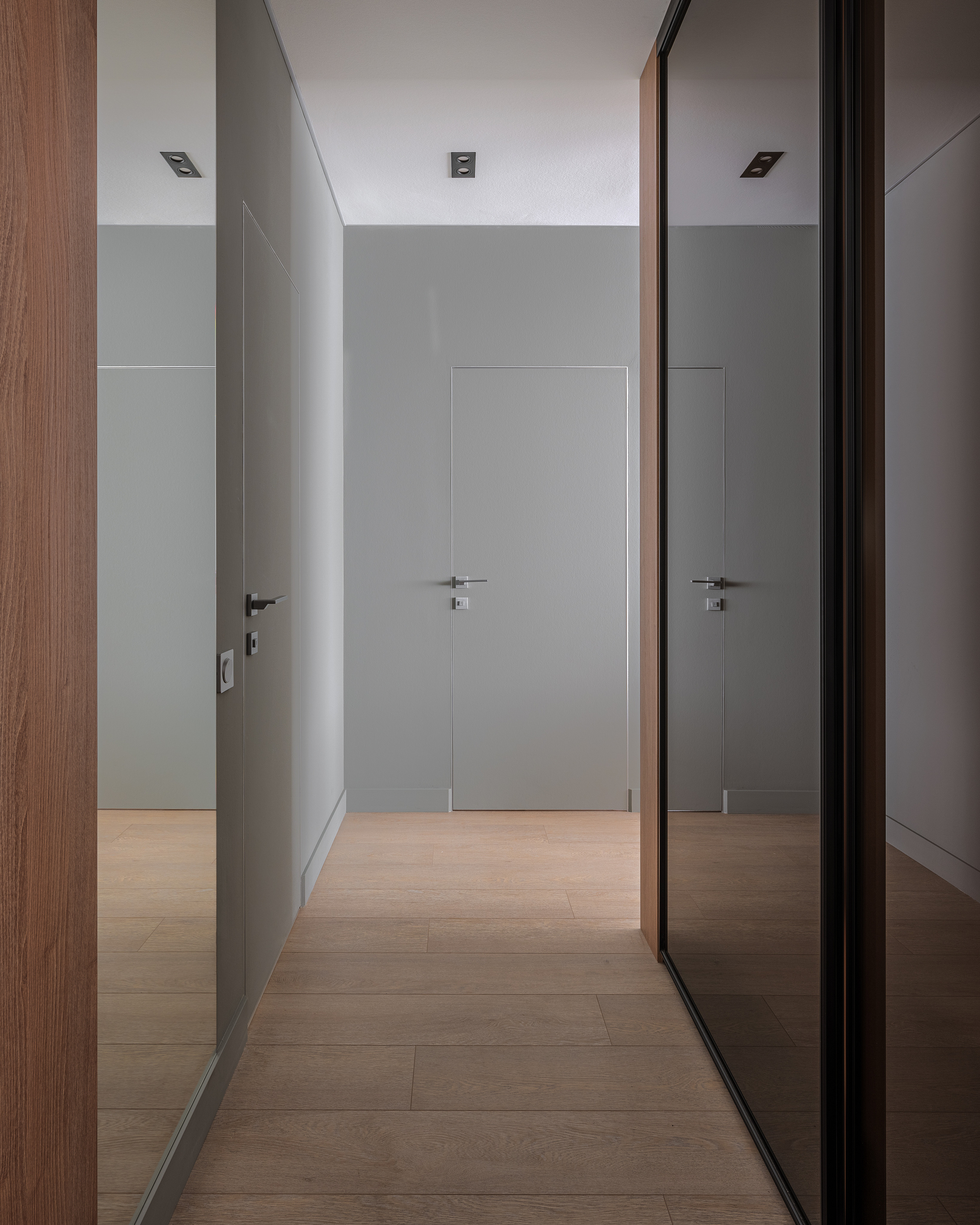 Минималистичный интерьер коридора с серыми дверями, встроенными ручками и деревянным паркетом в светлых тонах, гармоничное сочетание современного стиля от дизайнера Алёны Сверловой, фото Сергея Денисенко