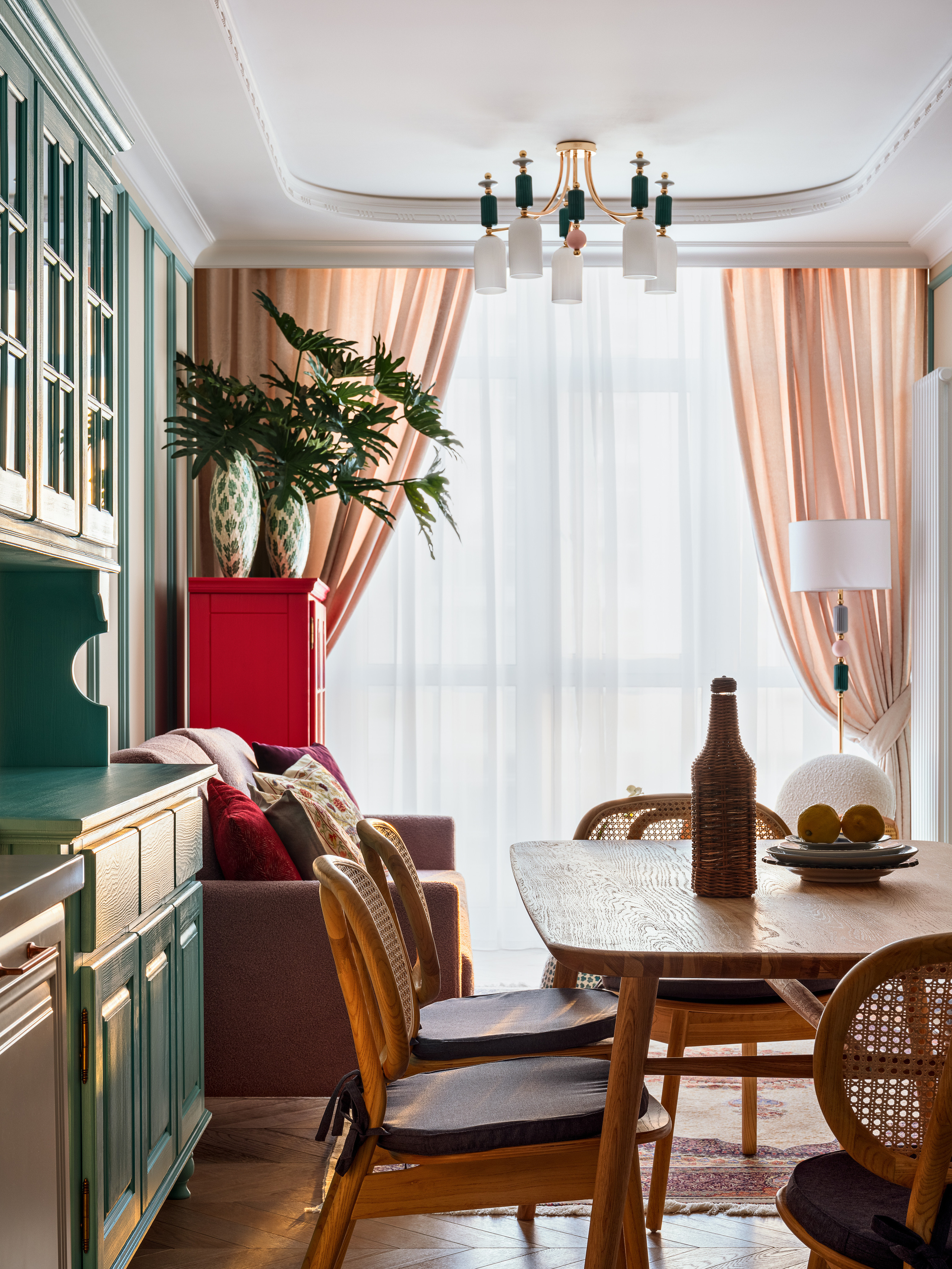 Столовая зона с деревянным столом, плетёными стульями и бирюзовым буфетом, за которым видна гостиная с диваном и пудровыми шторами у окна. Дизайнерский проект Оксаны Магомедовой, стилистика Натальи Якушевой, фото Сергея Денисенко.