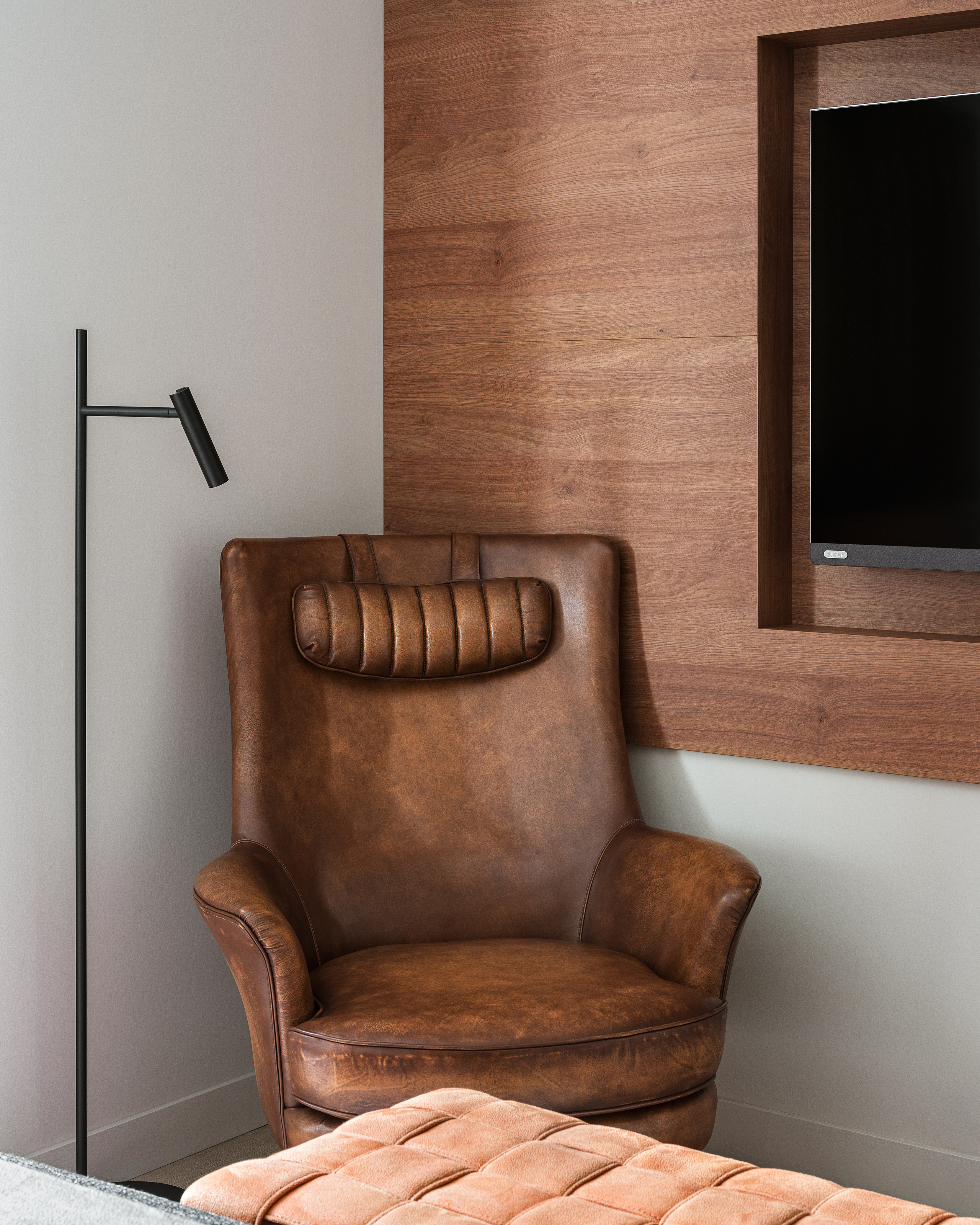 Лаконичная спальня с акцентной стеной из дерева, встроенным телевизором и удобным кожаным креслом с высоким подголовником. Дизайн реализован Алёной Сверловой, интерьер снят Сергеем Денисенко.