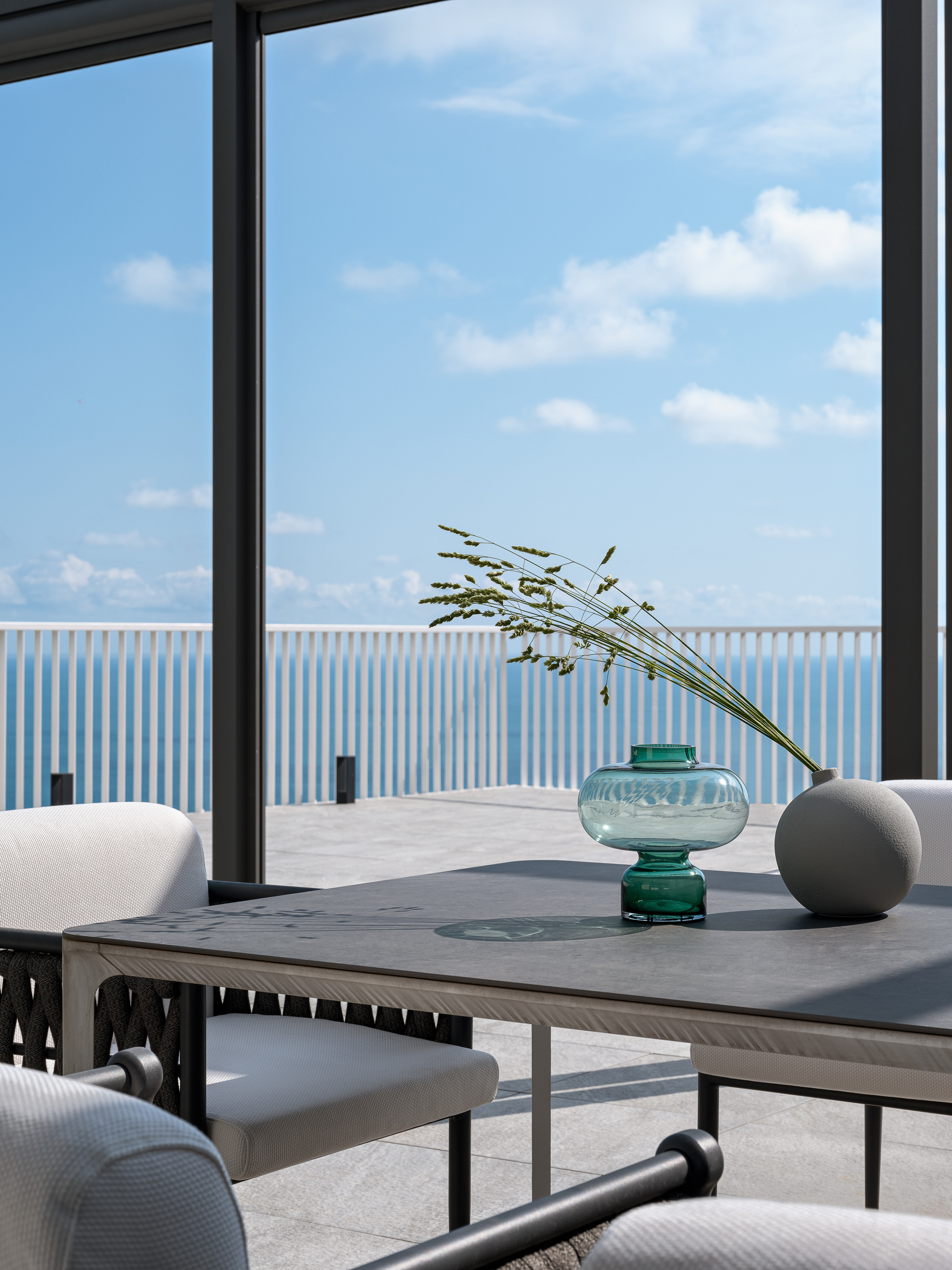 Современная терраса с панорамным видом на море, стильный стол с декоративной вазой из стекла и минималистичные кресла в светлой обивке; гармоничный интерьер подчеркнут стилистом Екатериной Ракитиной, фотограф Сергей Денисенко.