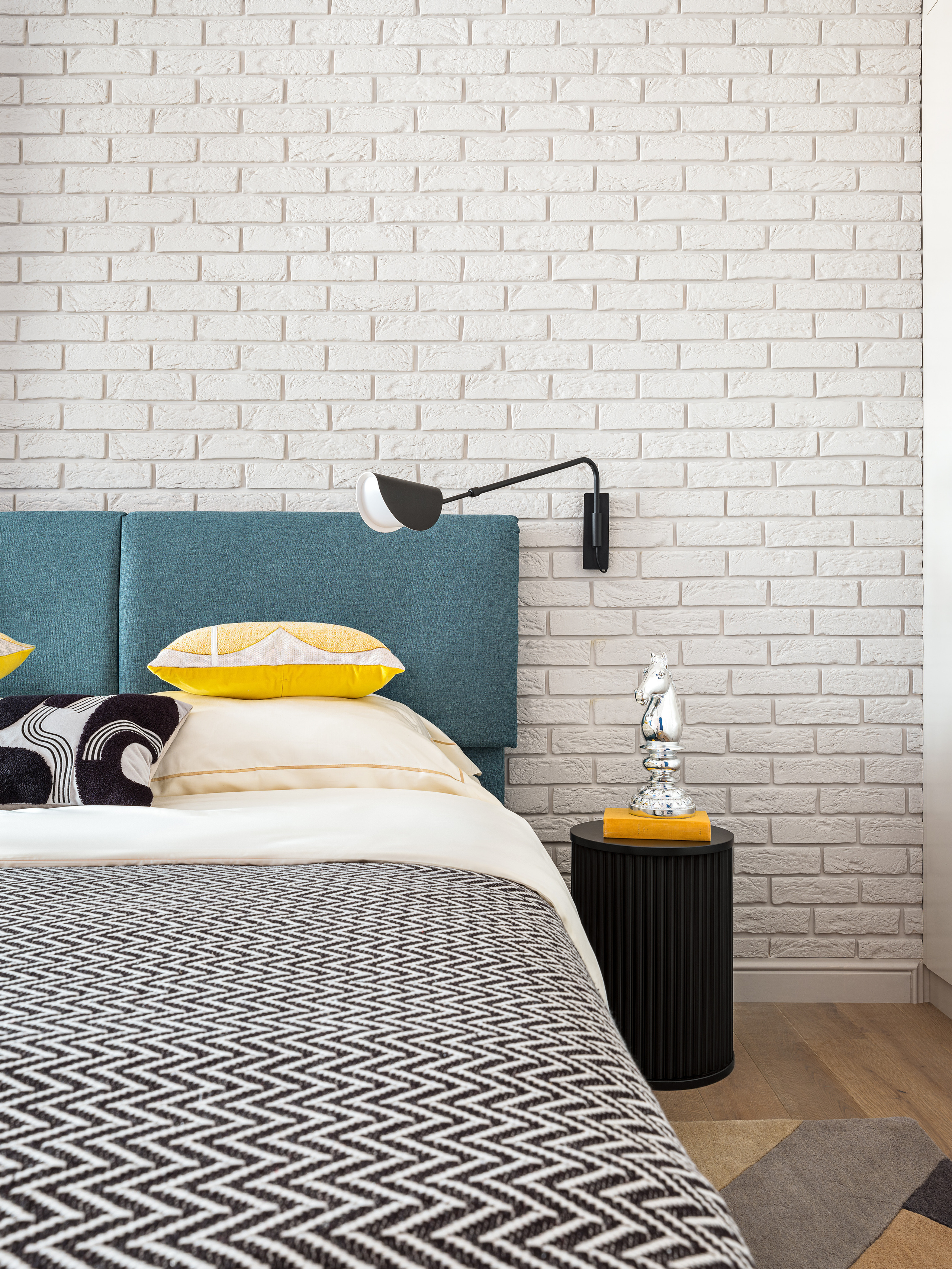 Дизайнерская спальня с белой кирпичной стеной, мягким изголовьем кровати в бирюзовой обивке, желтыми подушками и графичным покрывалом. Автор интерьера Оксана Магомедова, стилист Наталья Якушева, фотограф Сергей Денисенко.