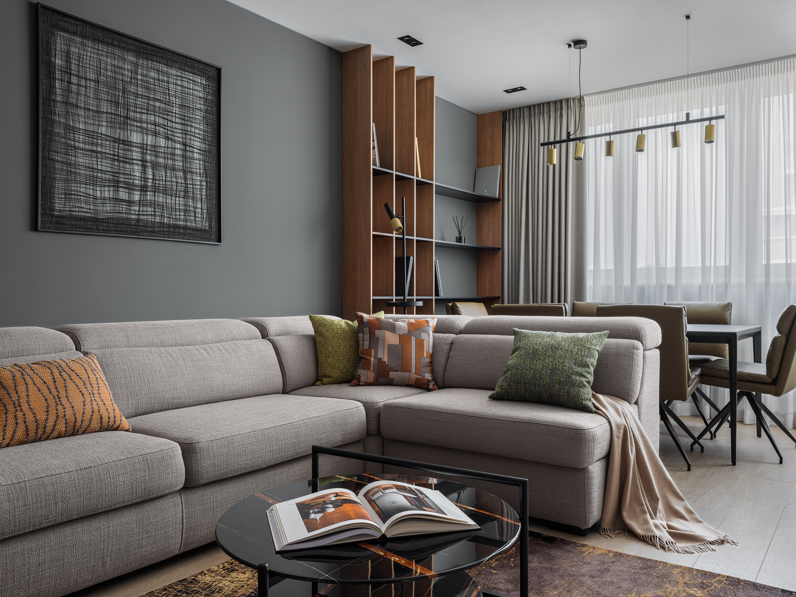 Современная гостиная с большим серым диваном, декоративными подушками и журнальным столиком из стекла, акцентными деревянными стеллажами и графичным декором на стене. Дизайнер интерьера Алёна Сверлова, фотограф Сергей Денисенко.