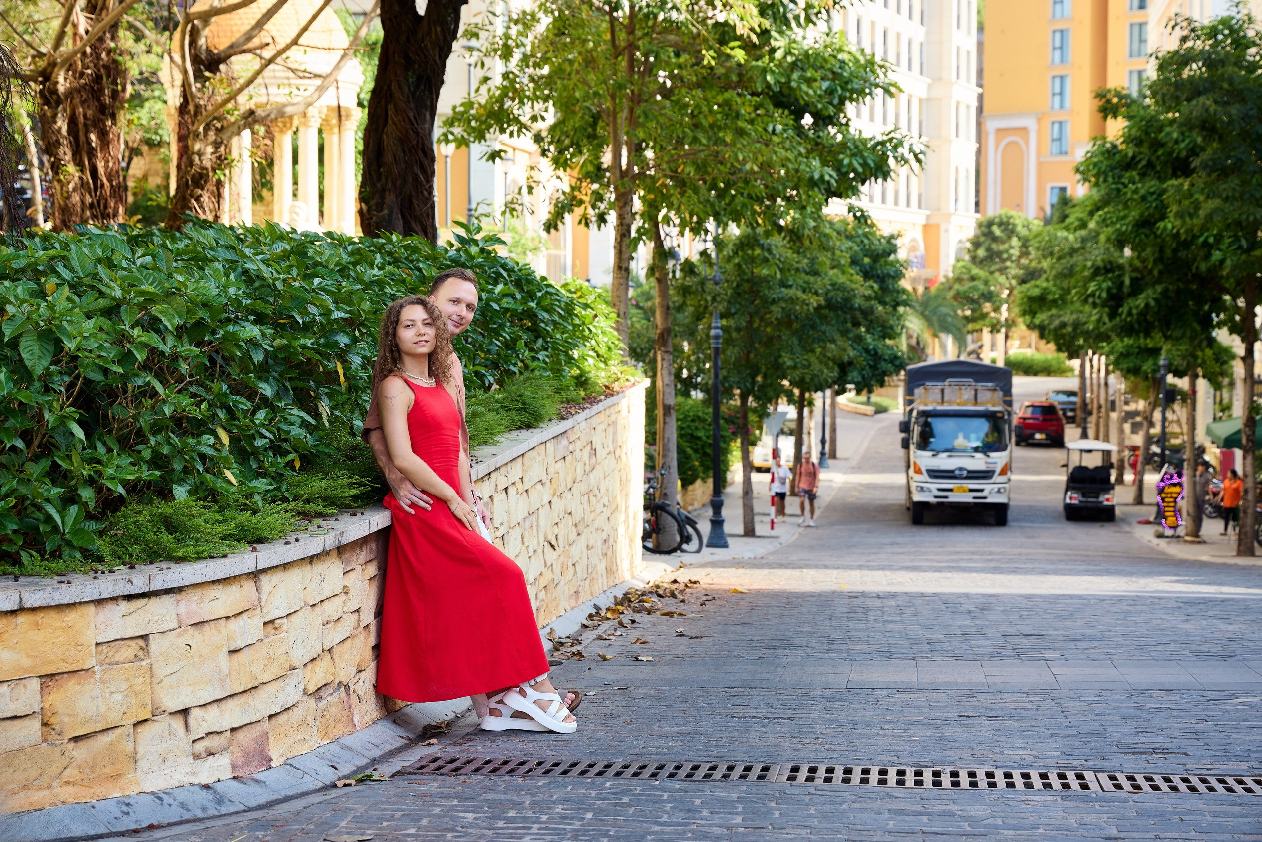 A couple in red and white clothes standing by a stone wall on a cobblestone street in the Mediterranean-style Sunset Town, Phu Quoc, Vietnam.