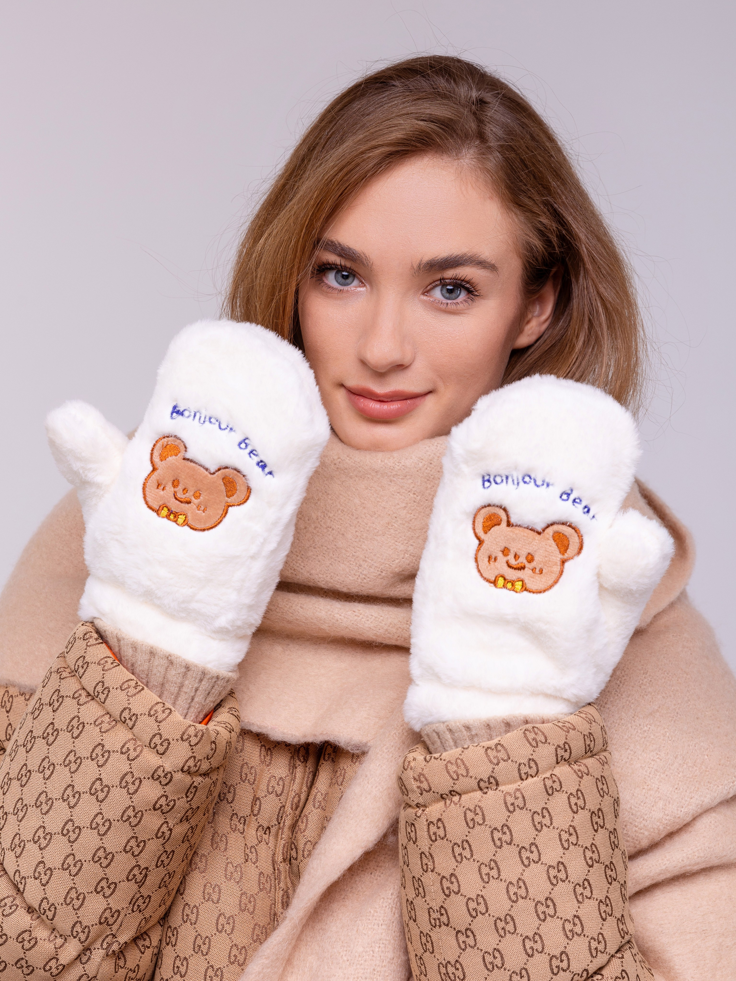 Девушка демонстрирует белые пушистые рукавицы с детской аппликацией.