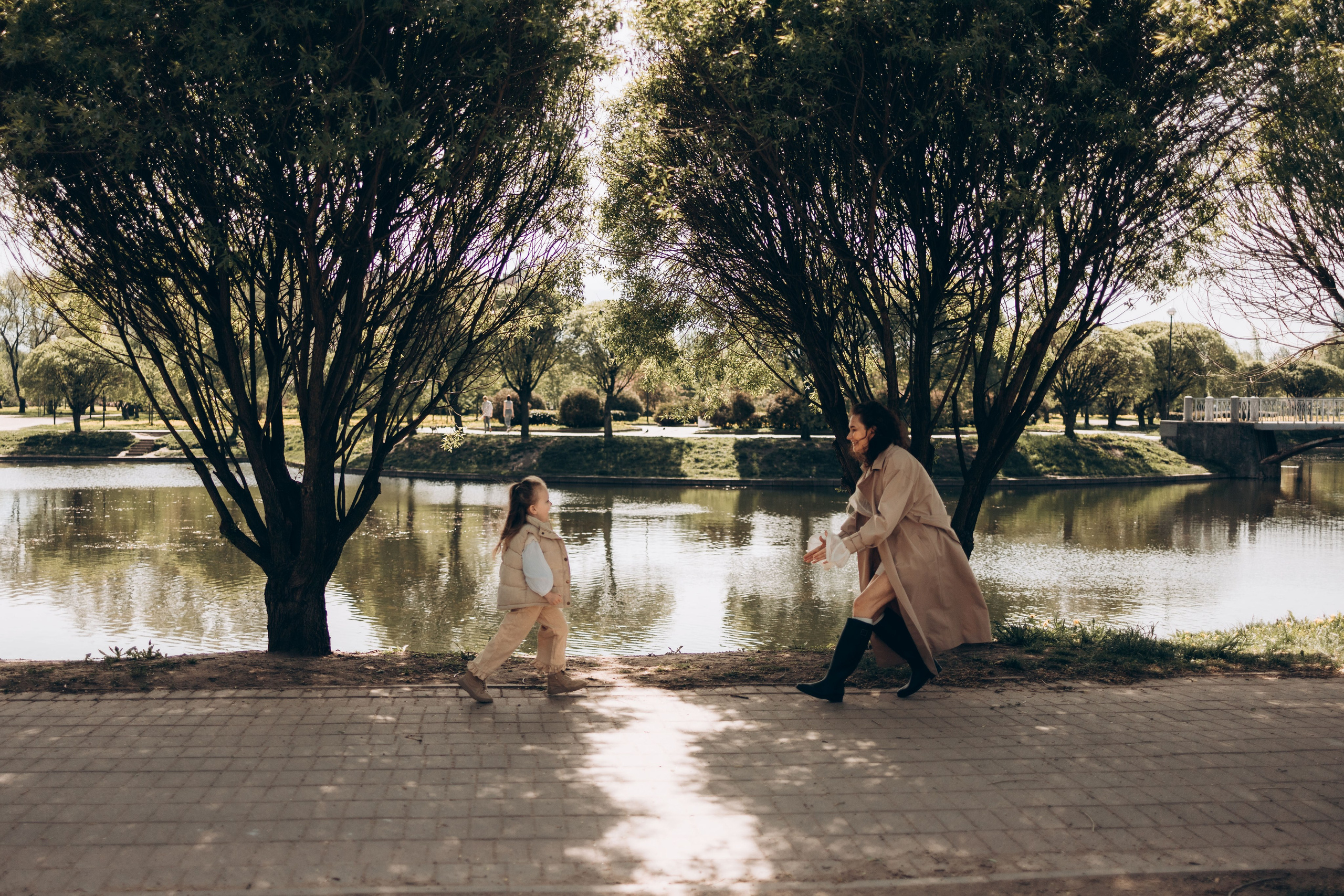 мама с дочкой бегут друг к другу в парке возле озера