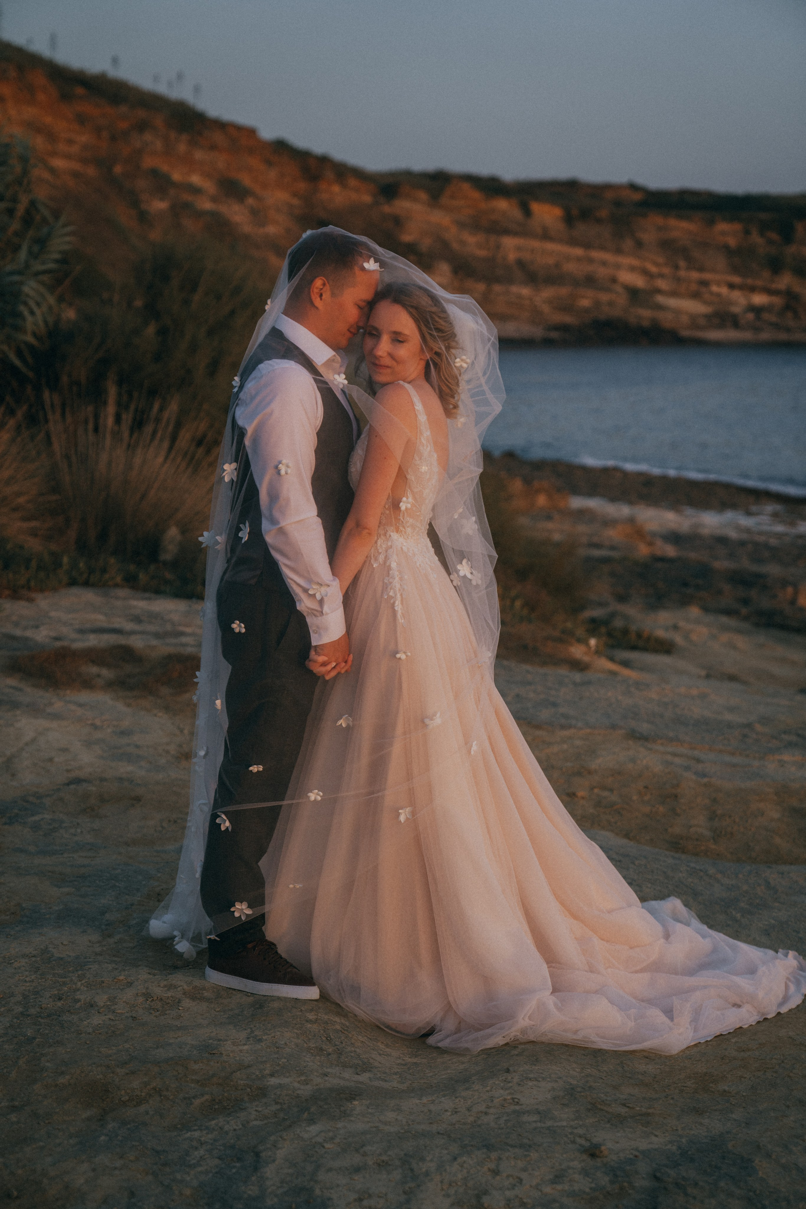 Счастливая пара жених и невеста целуется на фоне волн  скал и заката у моря океана.