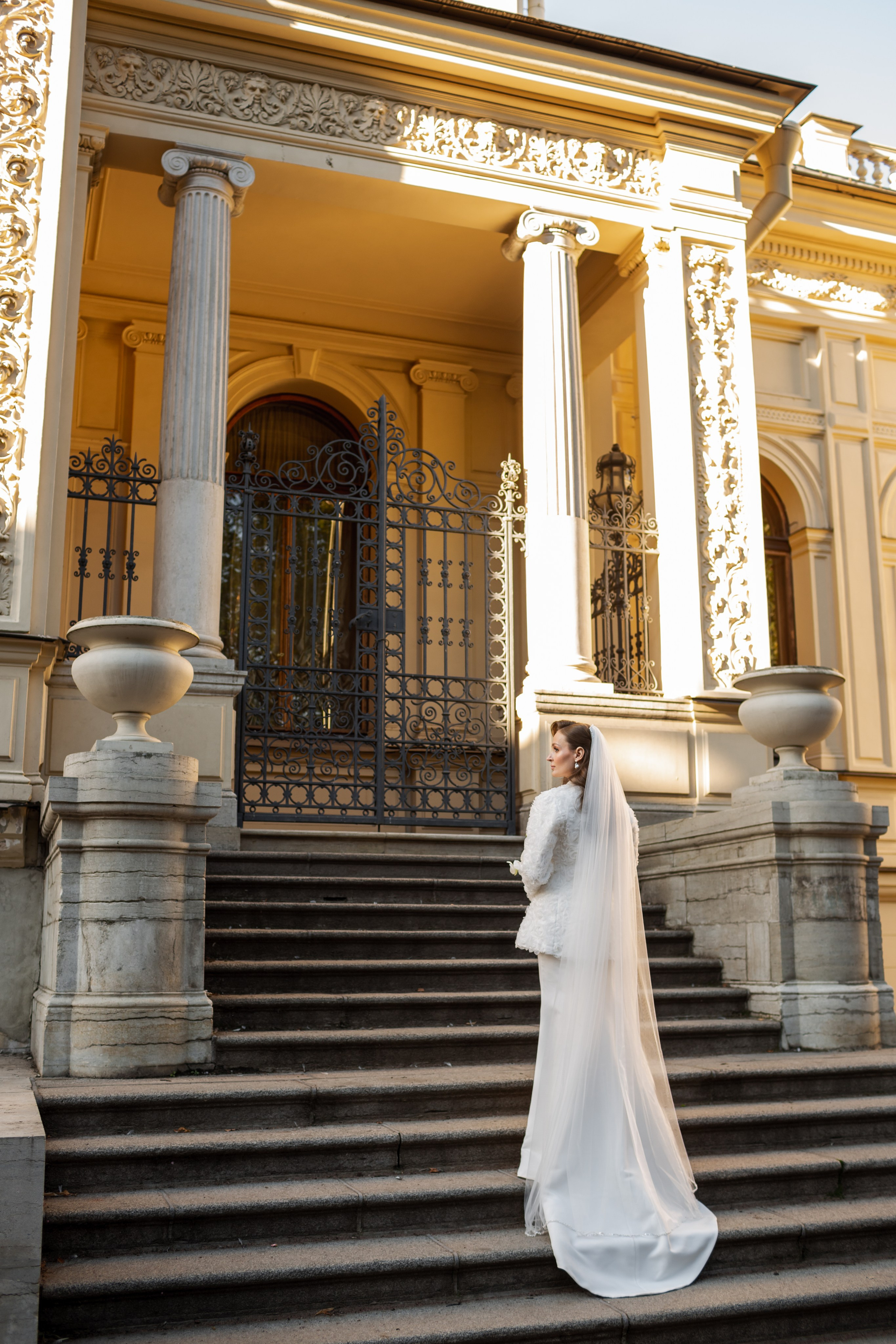 Невеста в белом платье со шлейфом и разрезом на лестнице старинного особняка.