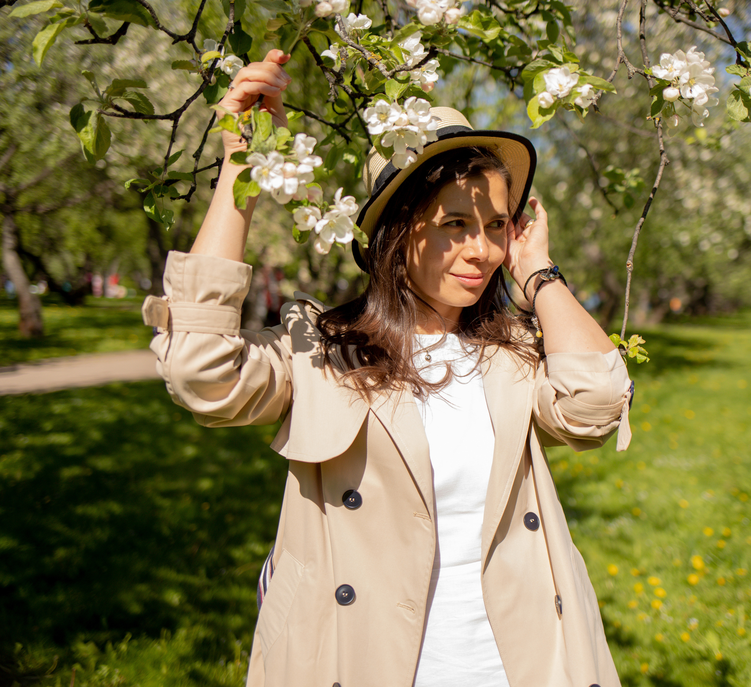 Девушка стоит у цветущей яблони в шляпе 