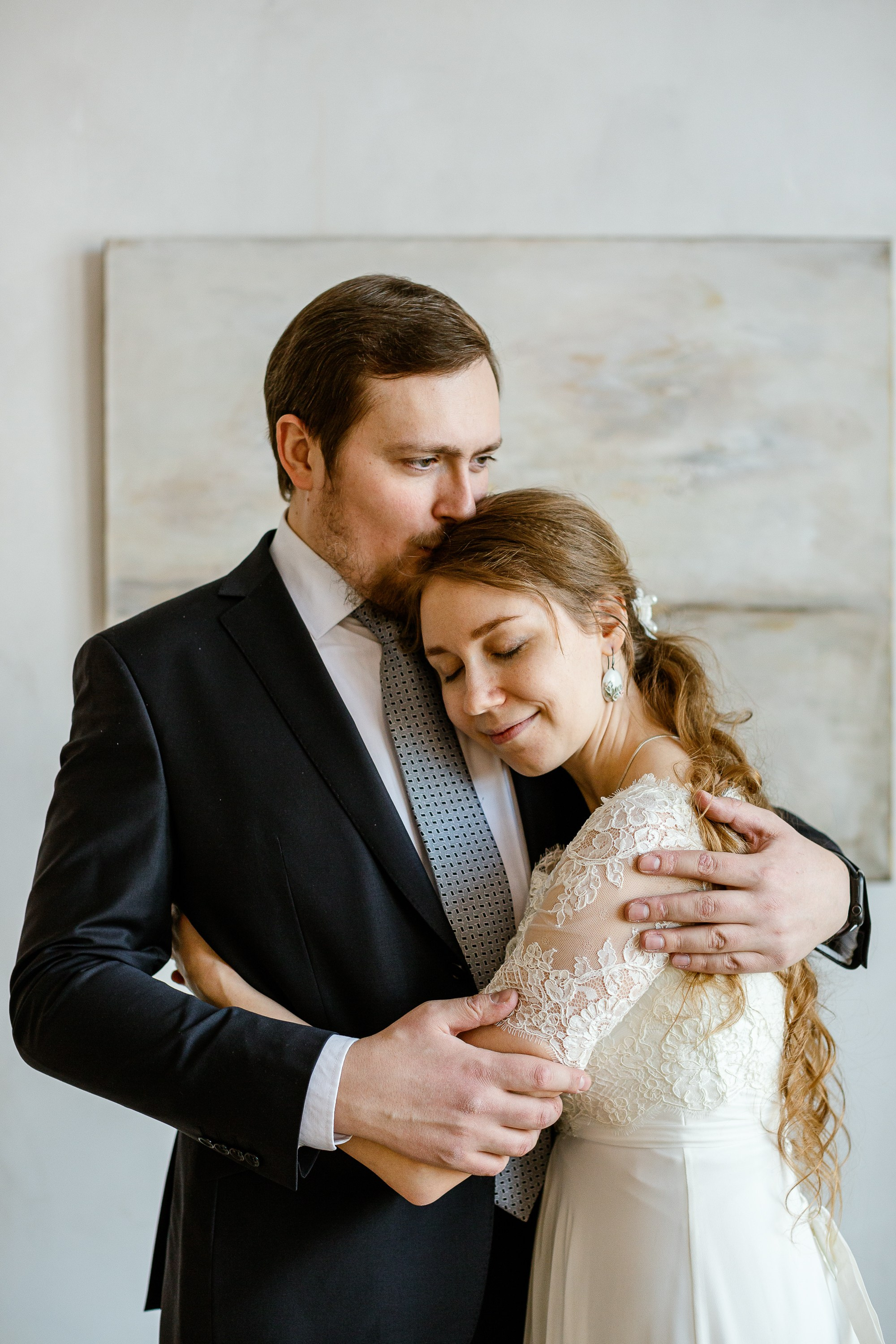 Жених и невеста в праздничной фотостудии. Жених в костюме, невеста в красивом белом платье. На фоне картина.