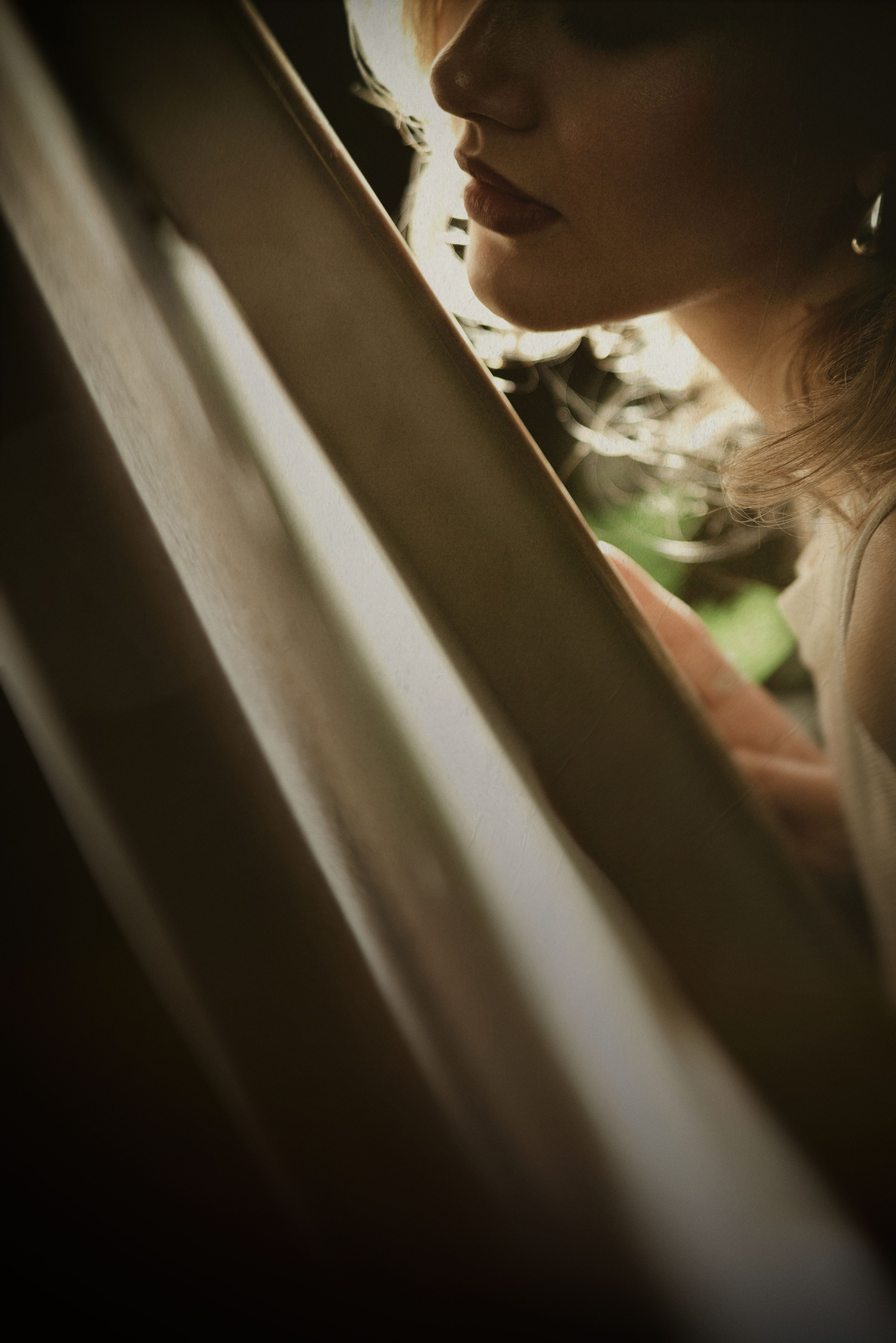 Интимный арт-портрет: крупный план лица девушки за деревянными жалюзи, мягкий естественный свет, художественное размытие