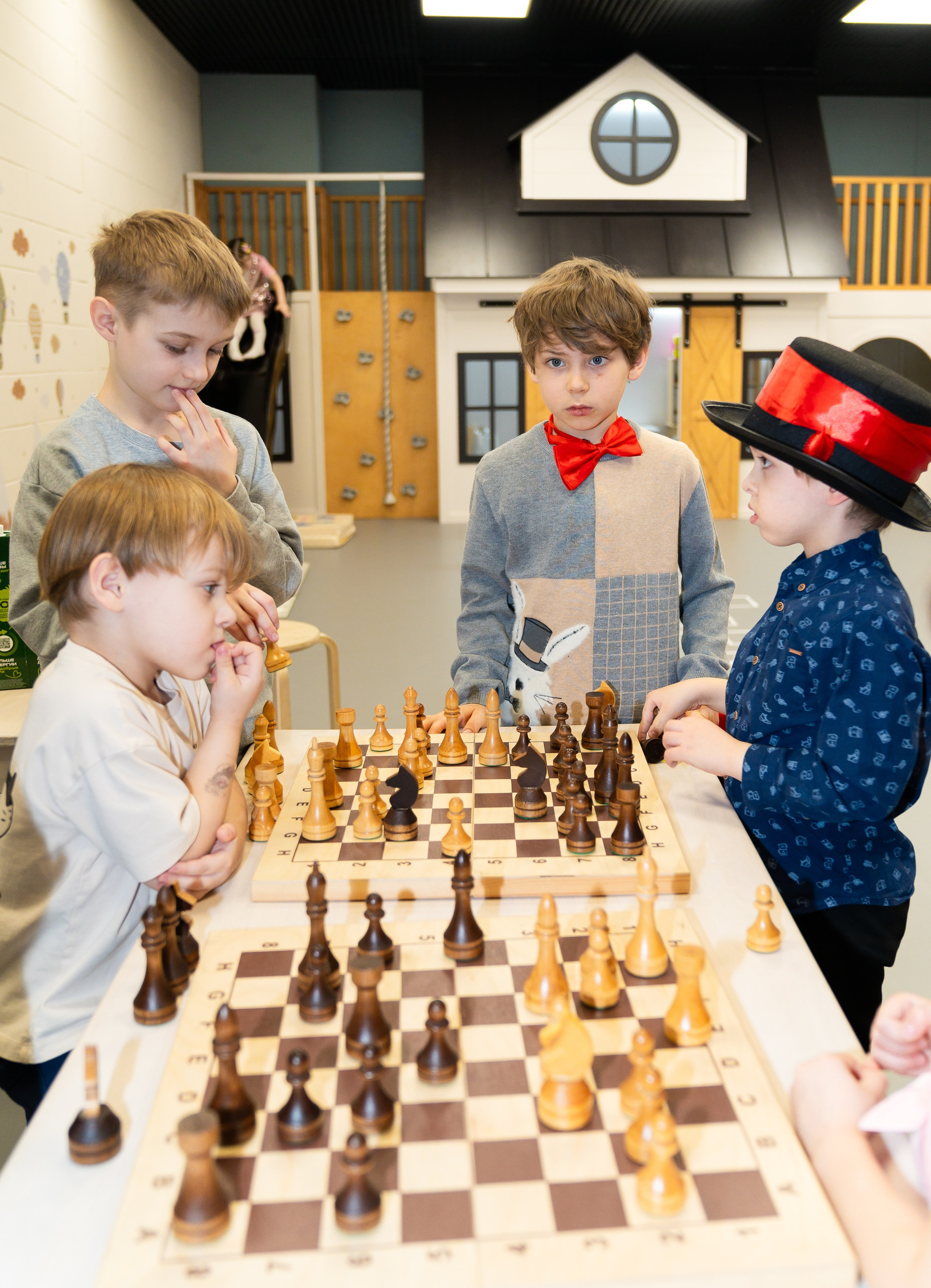 Группа мальчиков в шляпах и костюмах обсуждает ходы за шахматной доской в клубе Белая Королева Санкт-Петербург, детский шахматный праздник, фото Евгений Мальцев.