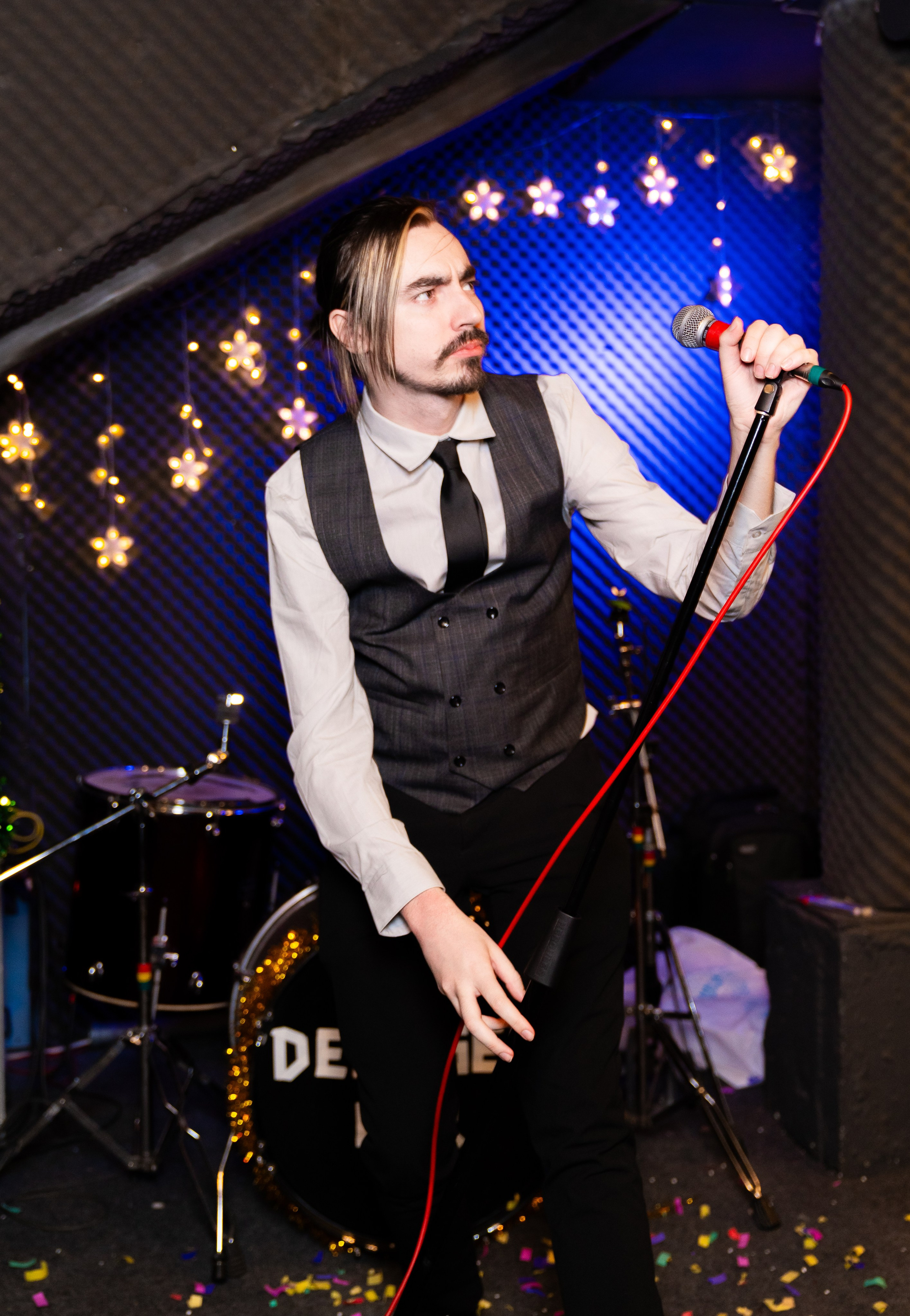 Мужчина в жилете с микрофоном на сцене бара Debaser во время новогодней вечеринки 2026 в Санкт-Петербурге. Фотограф Евгений Мальцев.