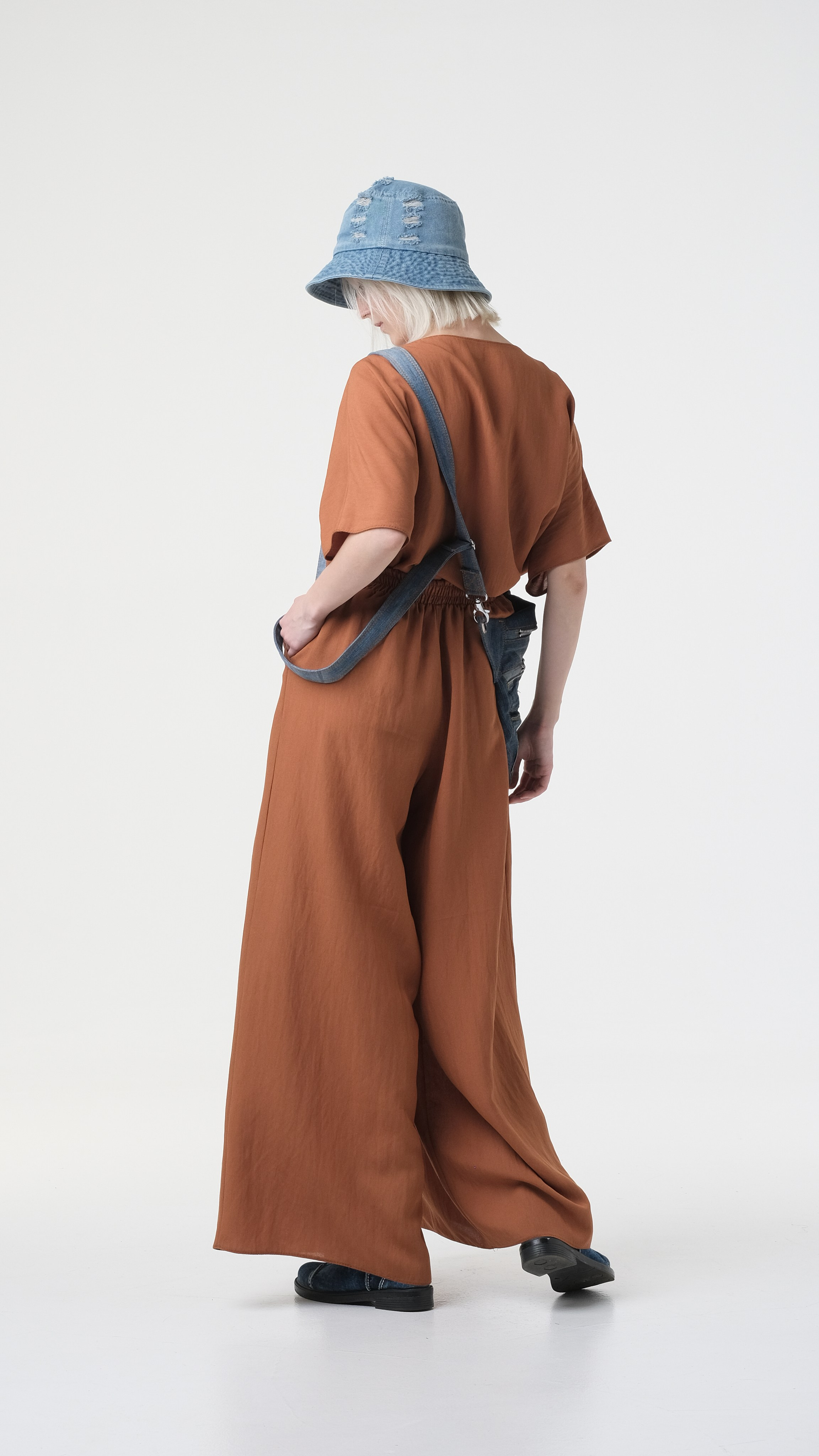 Модельное фото со спины на циклораме. На голове джинсовая панама, стильный брючный комплект.