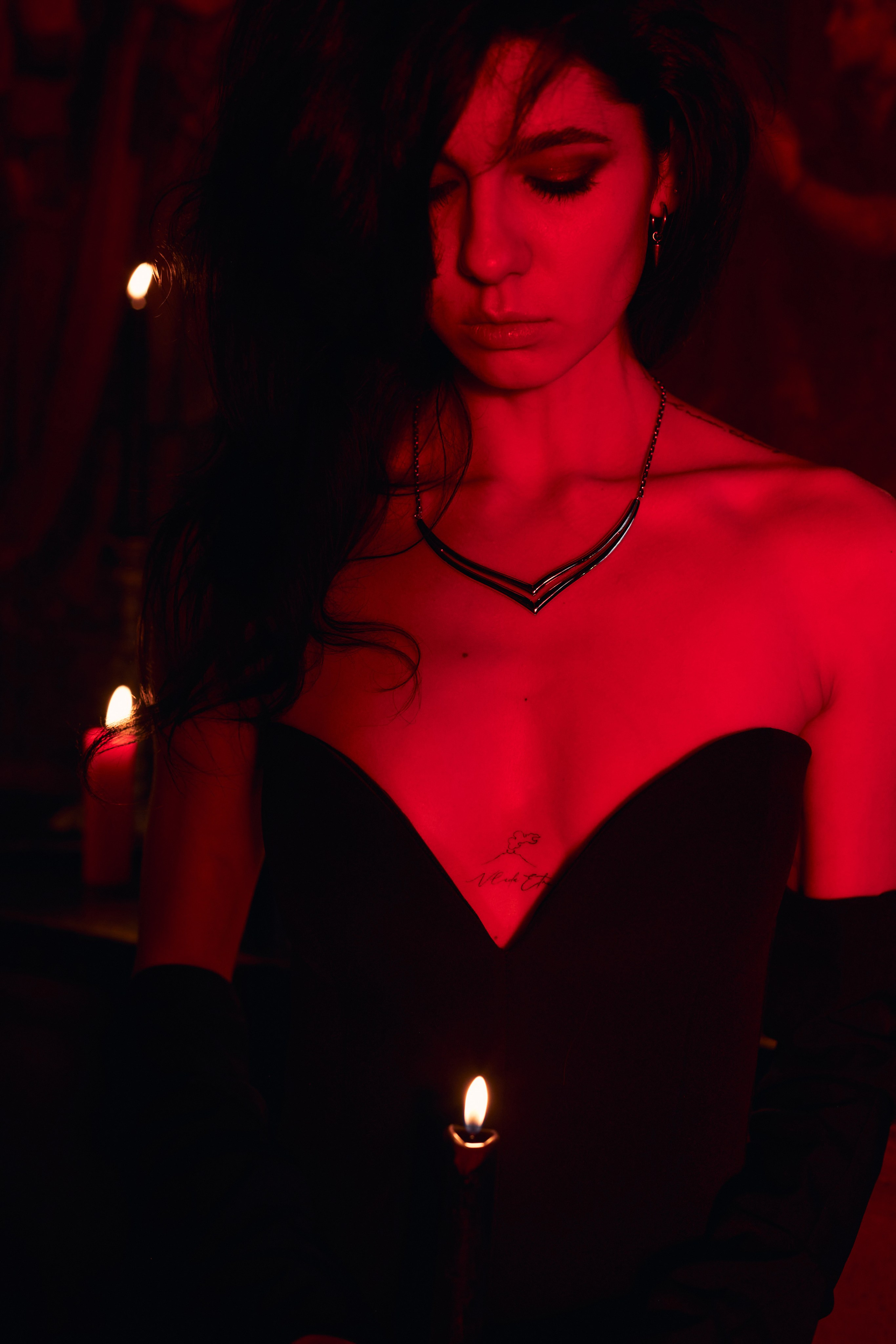 Девушка держит свечу на уровне груди. В разрезе платья видна татуировка