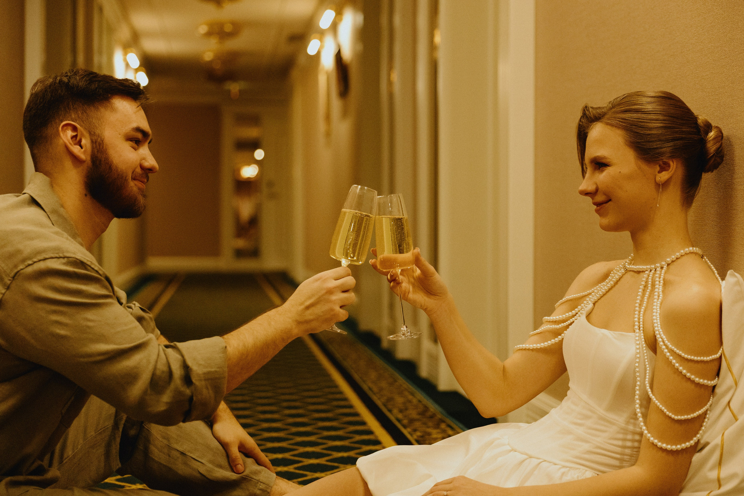 Жених и невеста сидят в коридоре, держа бокалы с шампанским.