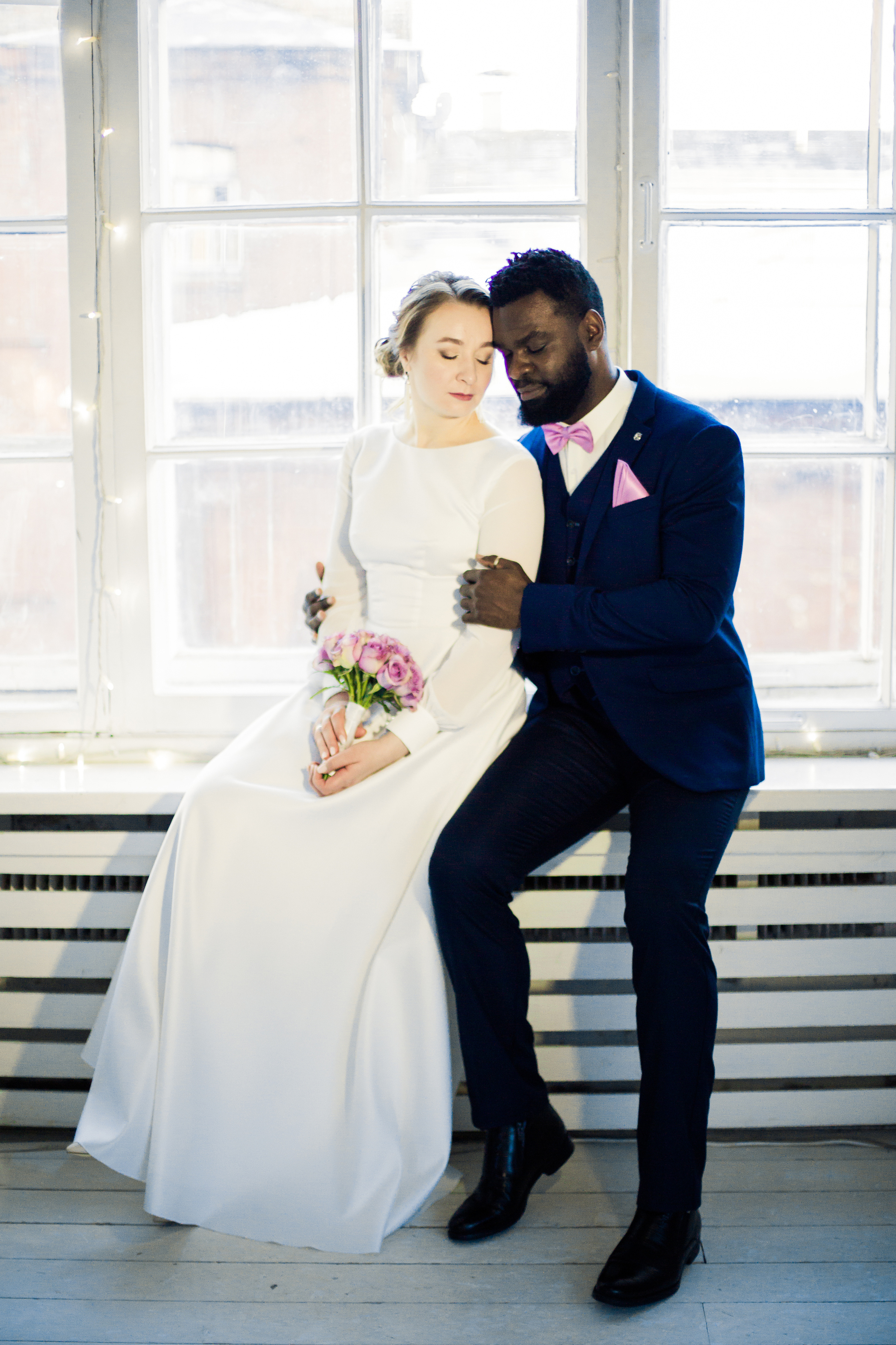 интернациональные жених и невеста на фоне зимнего окна с розовым букетом