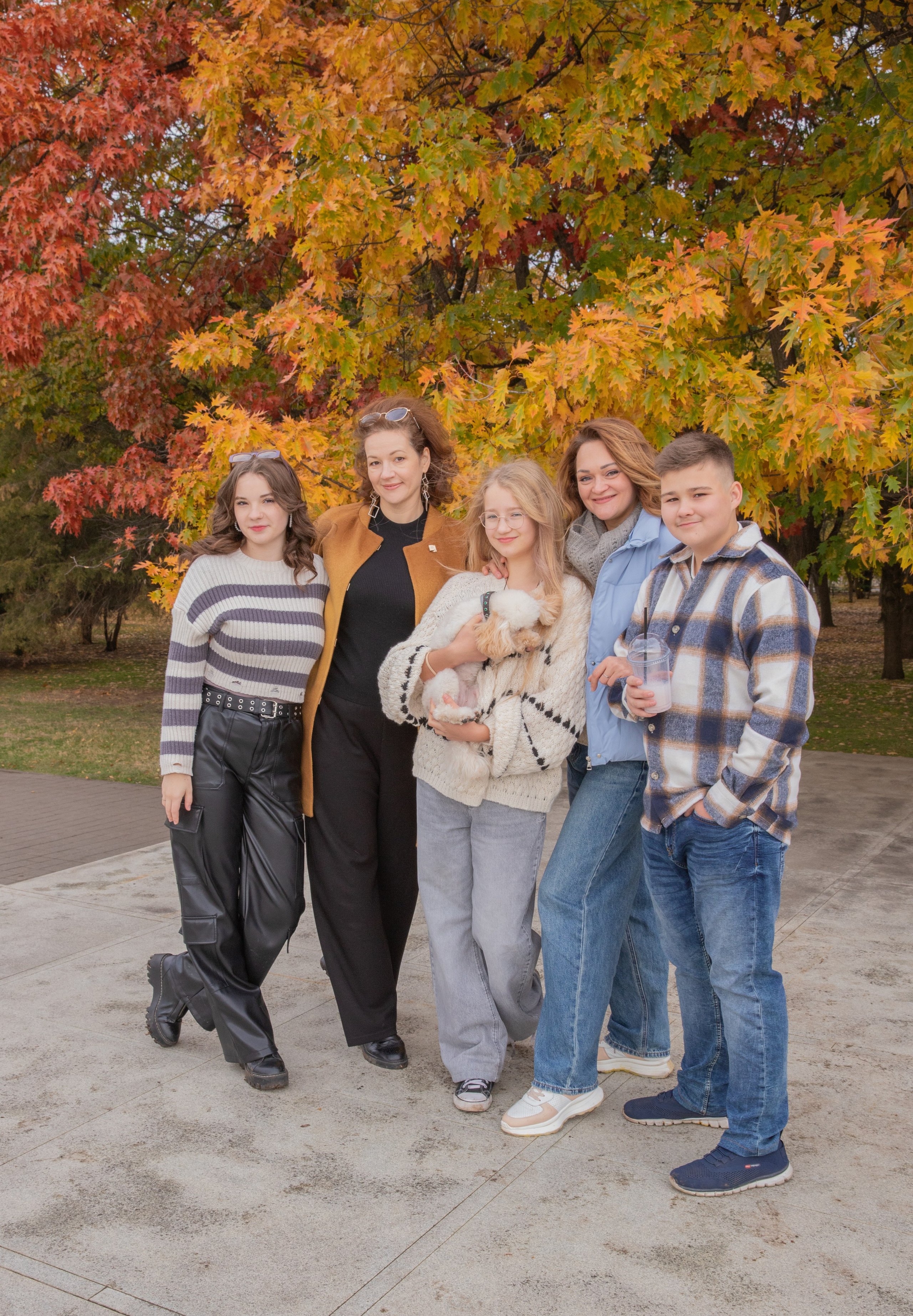 Друзья наслаждаются осенней прогулкой, окруженные золотистыми деревьями и падающими листьями.