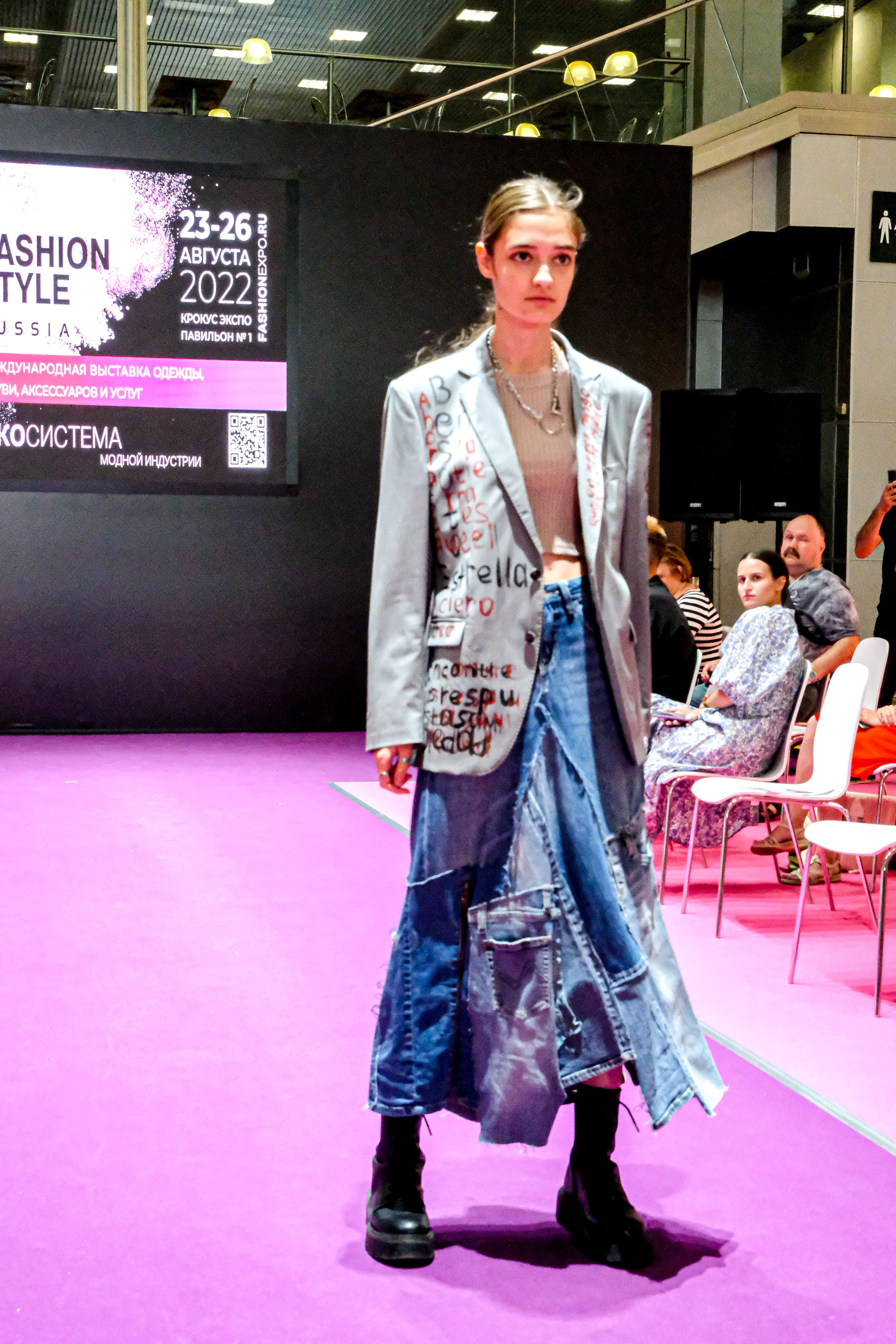  "Модели в ярких нарядах проходят по подиуму во время показа мод, освещенные яркими софитами и окруженные восторженными зрителями."