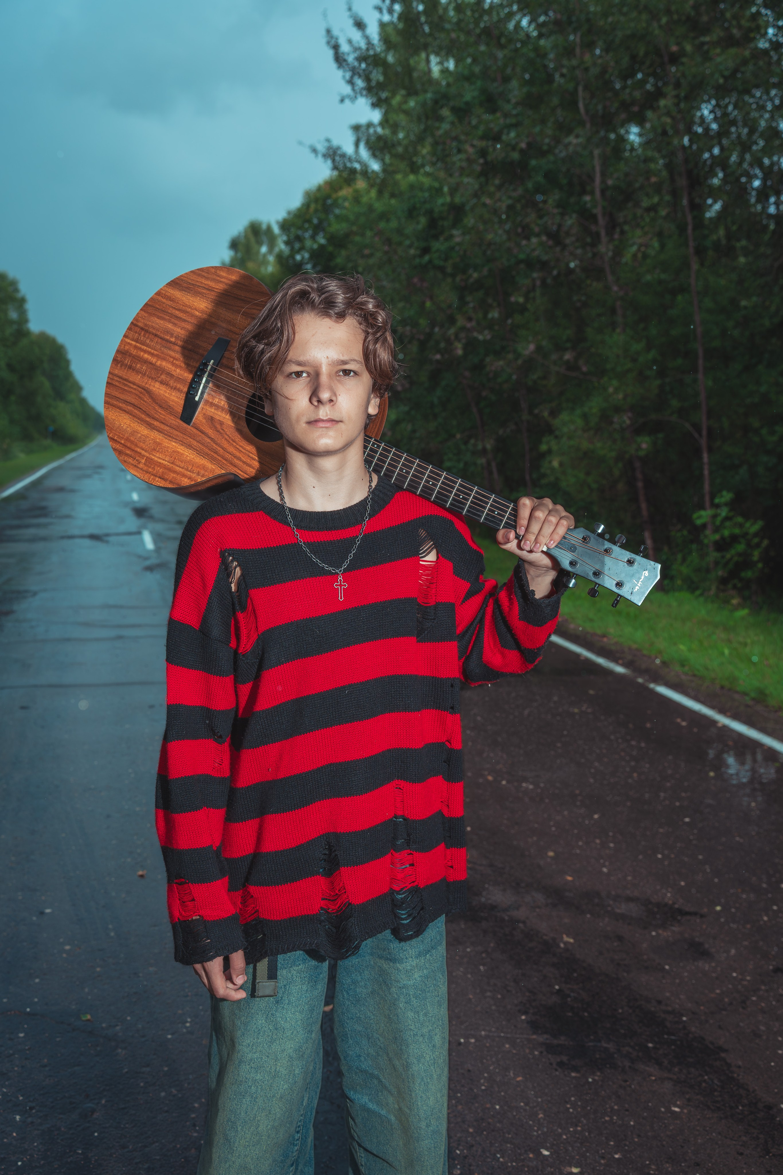 Молодой человек на дороге в стильной одежде с гитарой