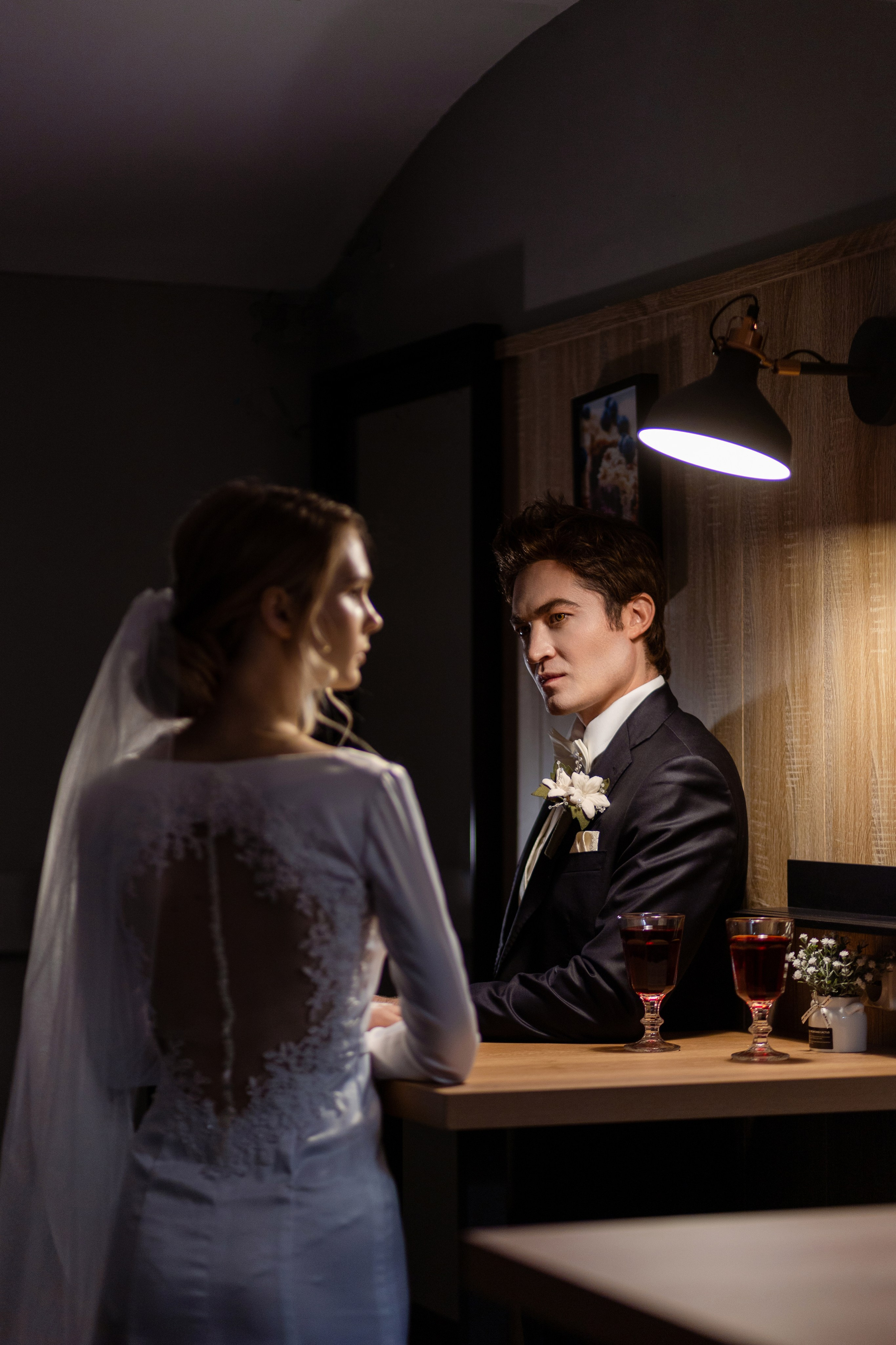 Над женихом, стоящим с невестой у стола Светит лампа.