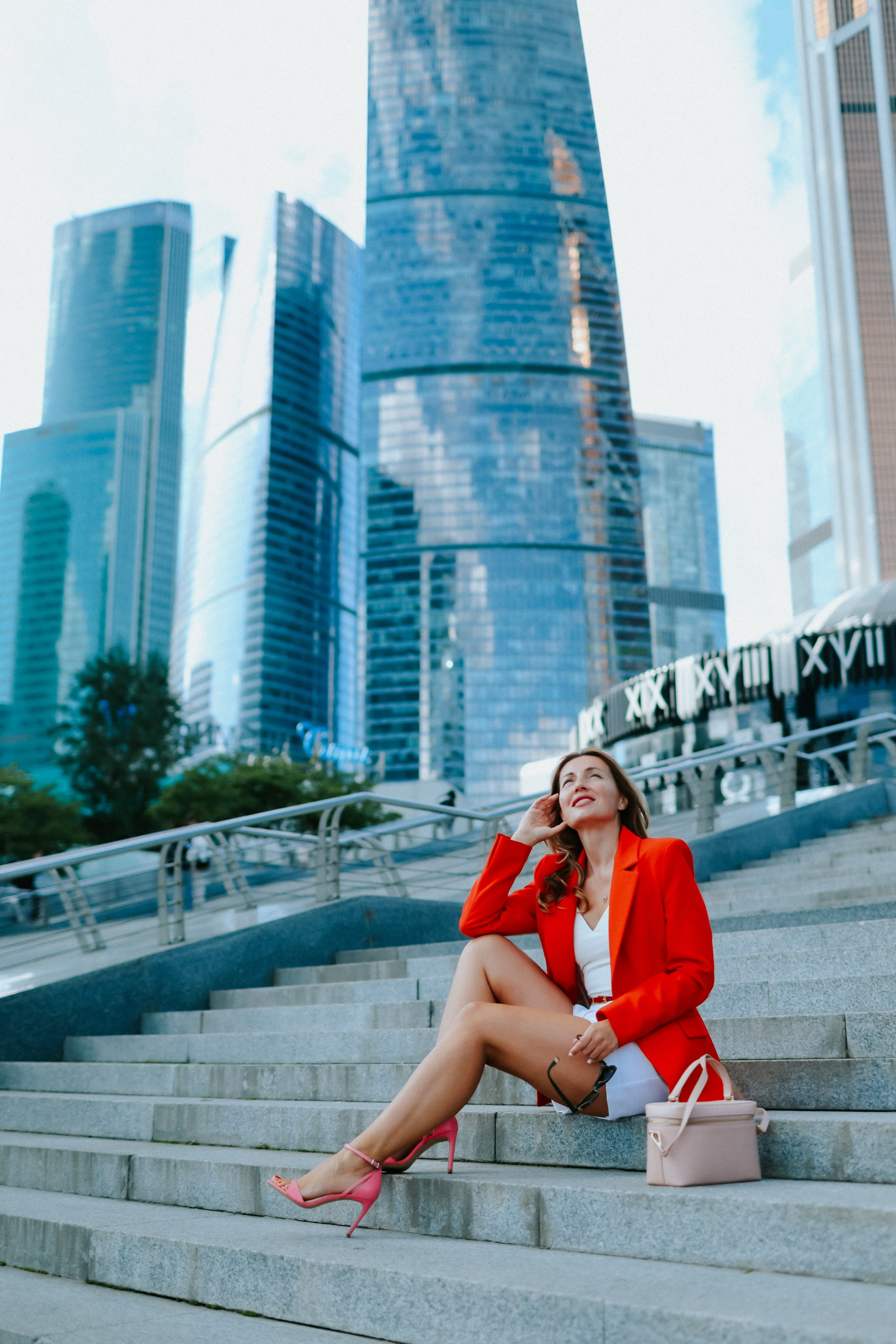 <img src="IZ0A0352.jpg" alt="Бизнес-леди успешная и красивая молодая девушка в в ярком красном пиджаке сидит на ступеньках  на фоне небоскрёбов Москва-Сити">