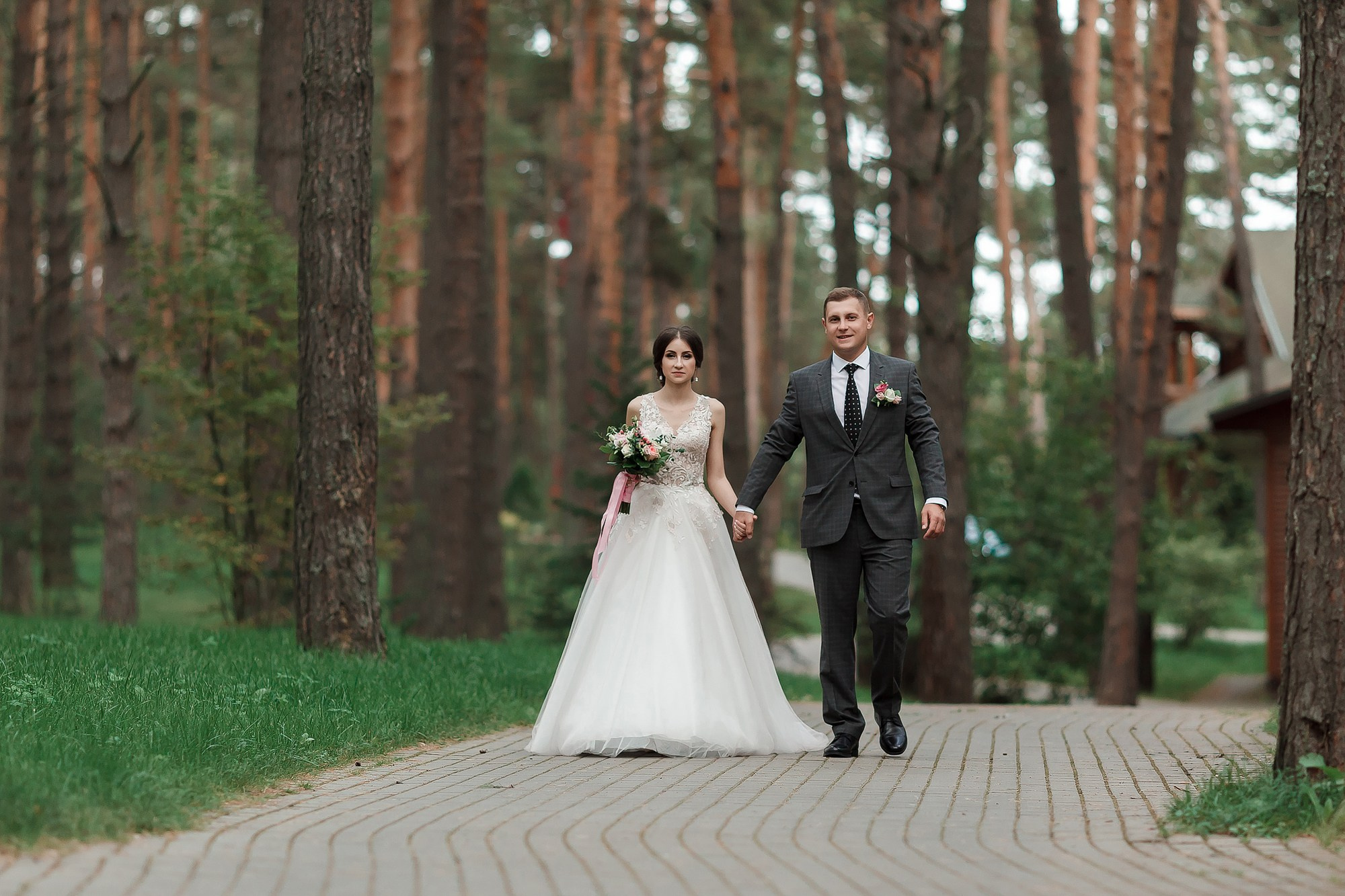 Жених и невеста прогуливаются по дорожке в лесу 