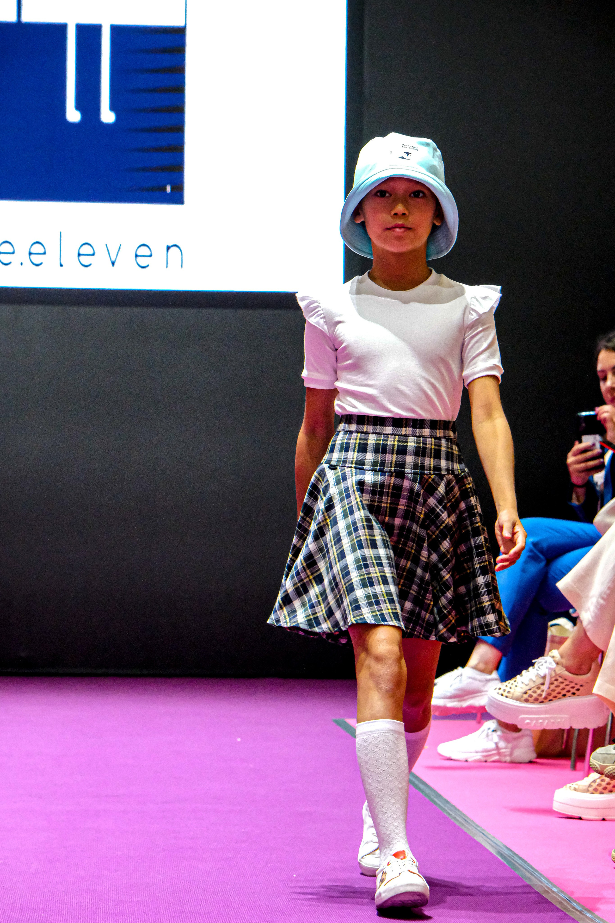  "Модели в ярких нарядах проходят по подиуму во время показа мод, освещенные яркими софитами и окруженные восторженными зрителями."