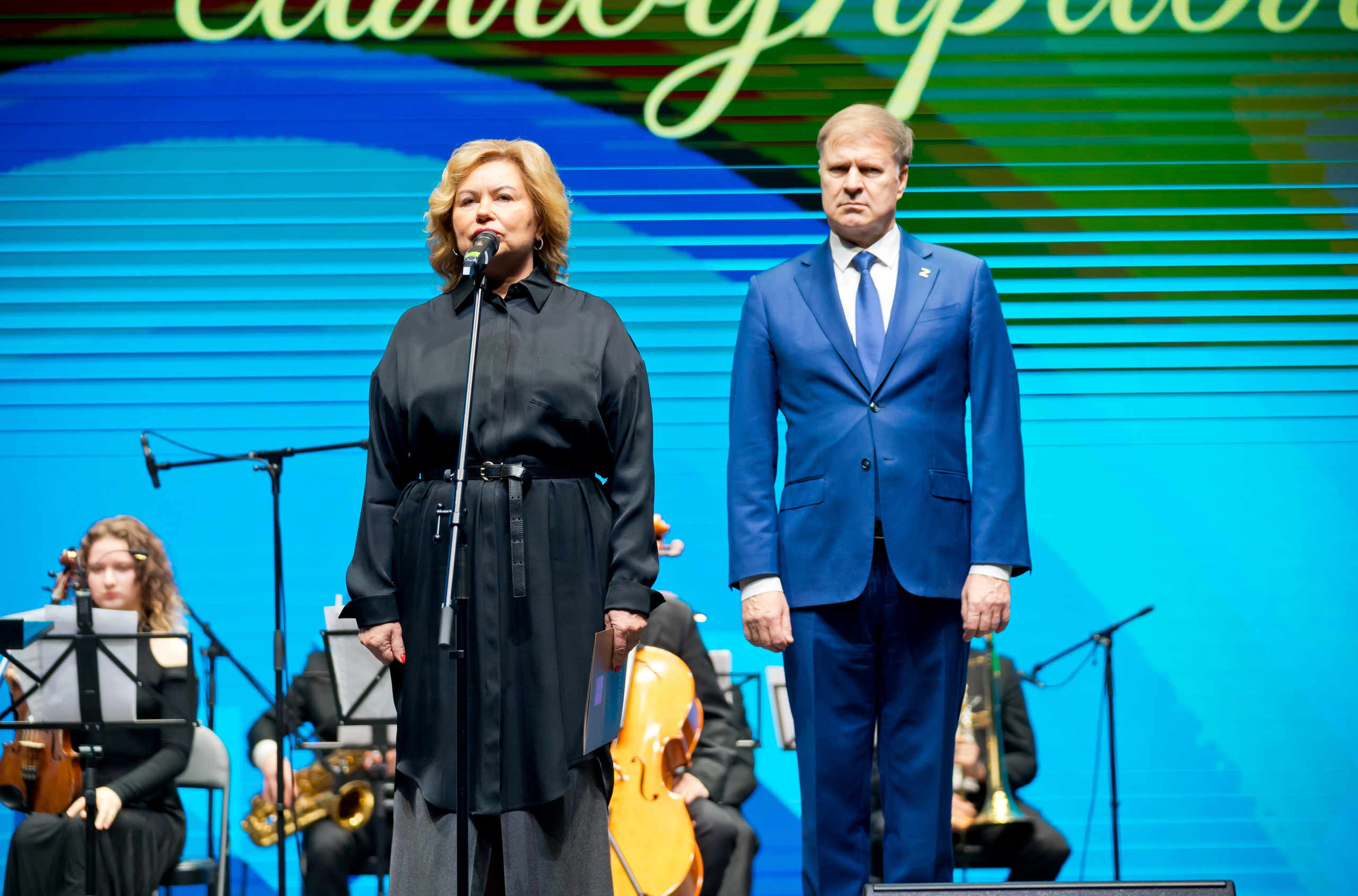 Женщина в чёрной блузке и мужчина в синем костюме стоят на сцене во время торжественной части. День местного самоуправления СПб. Фото Евгения Мальцева.