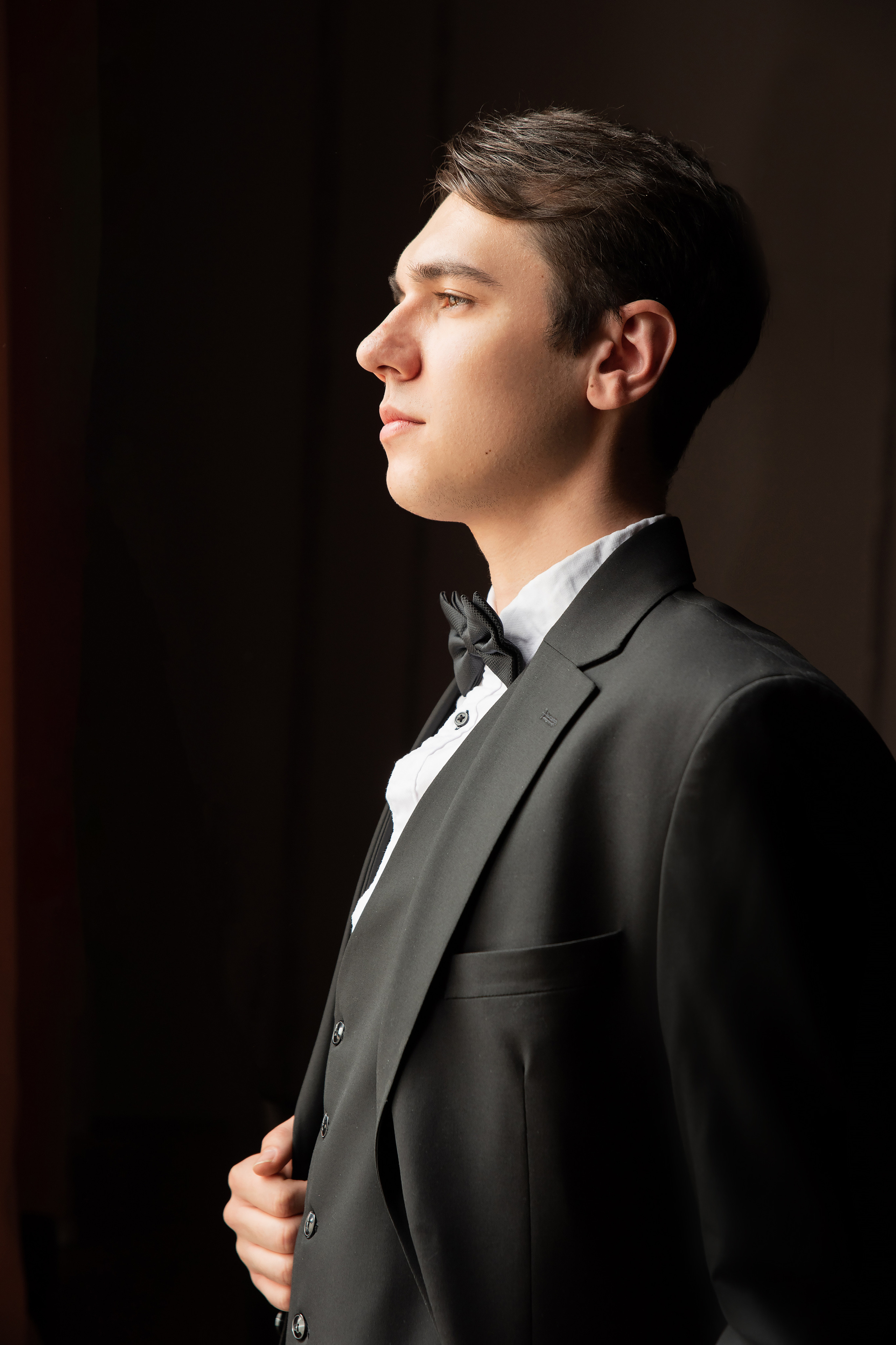 крупный портрет жениха в черном костюме у окна в профиль 