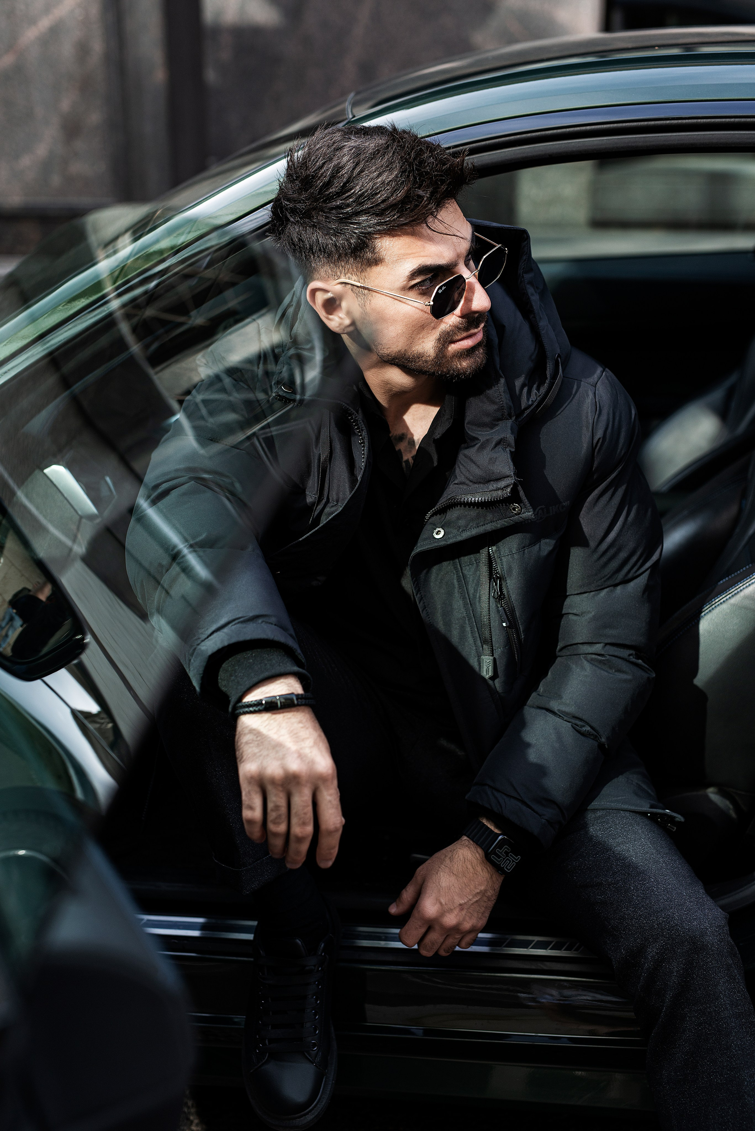 Брутальный и стильно одетый мужчина позирует сидя в BMW