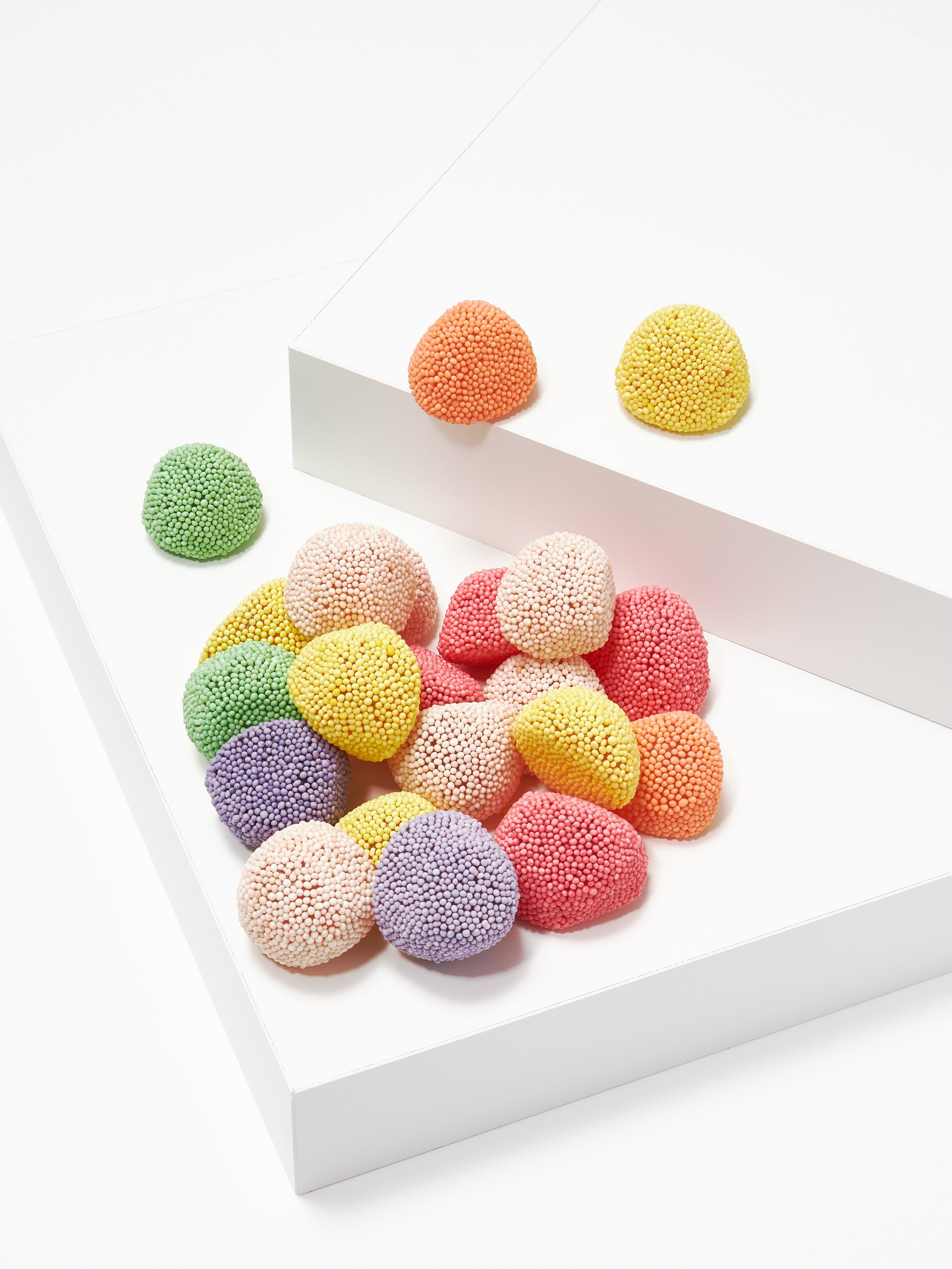 Каталожная предметная фотосъёмка разноцветного мармелада на белых подиумах на белом фоне