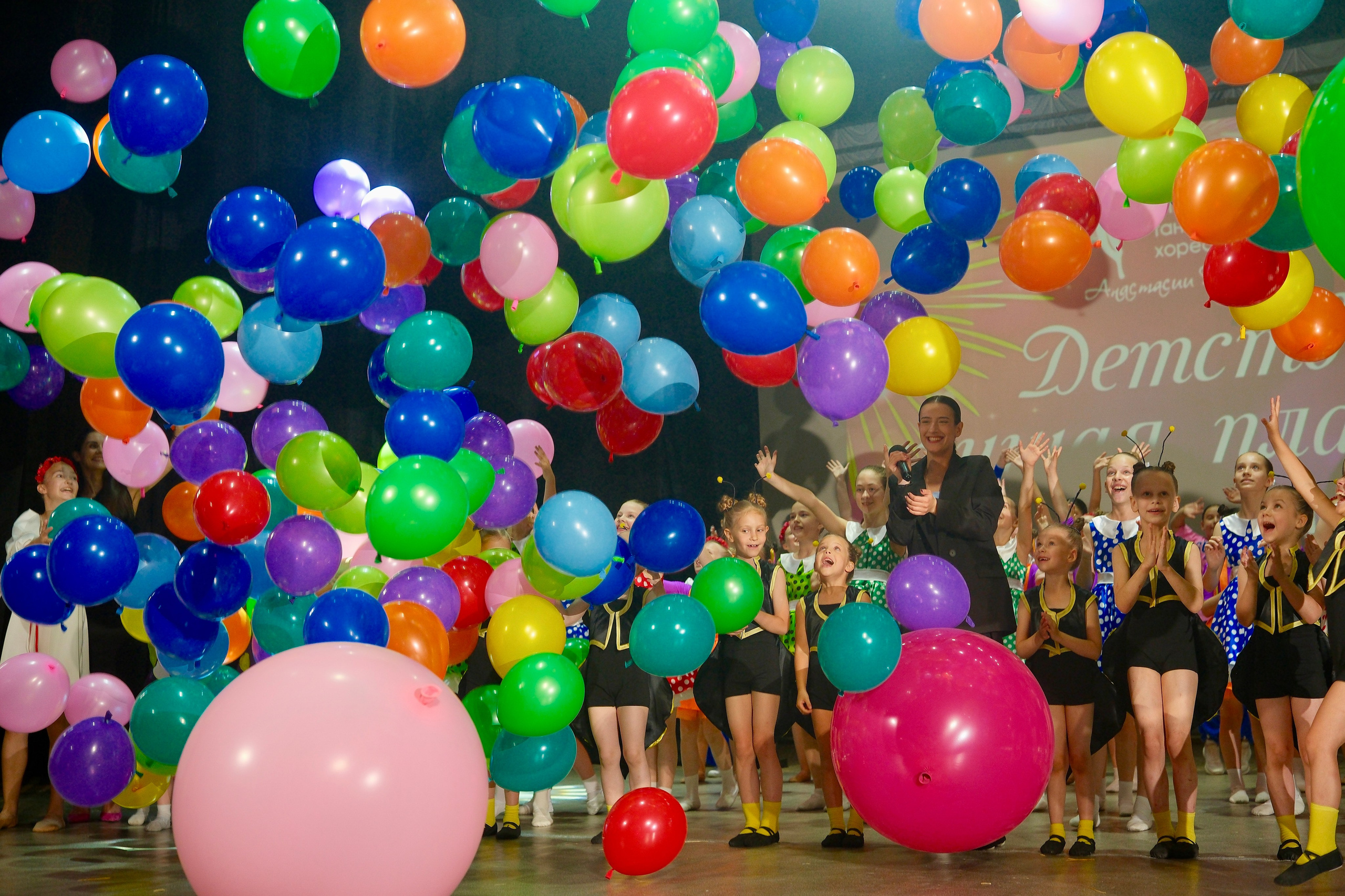 8-летняя солистка детского балета исполняет арабеск в белой пачке на сцене культурного центра