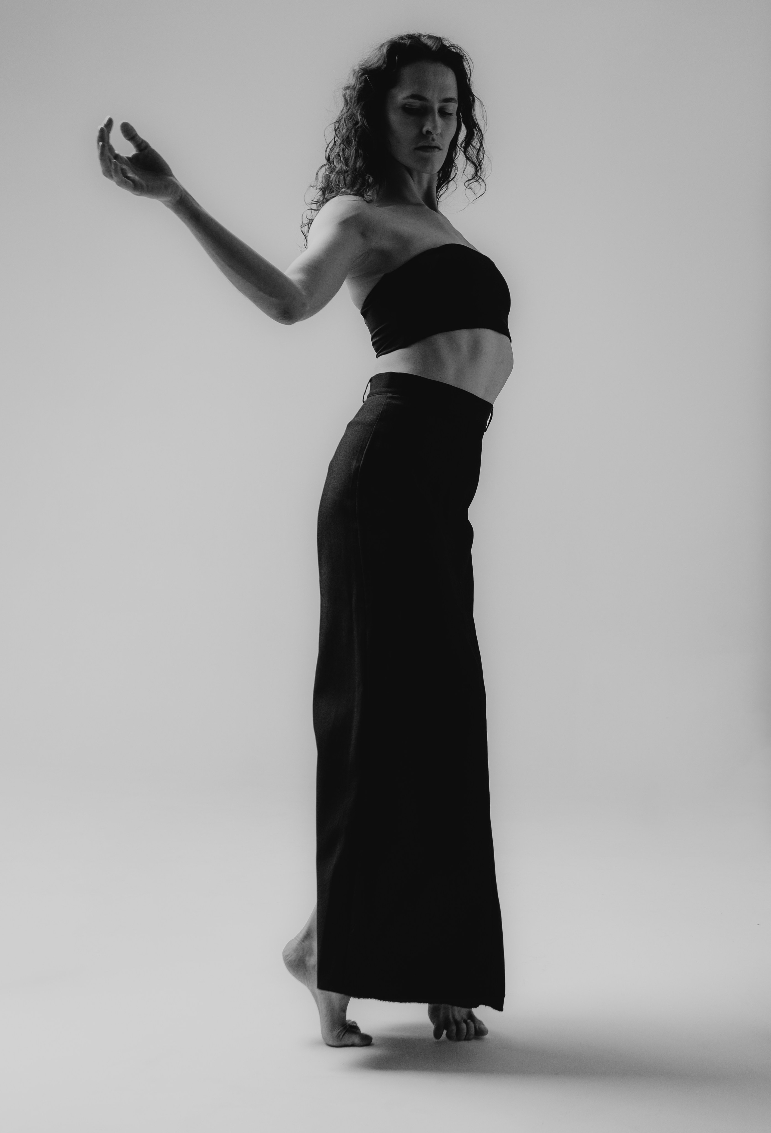 Девушка в чёрной юбке и чёрном топе танцует на циклораме