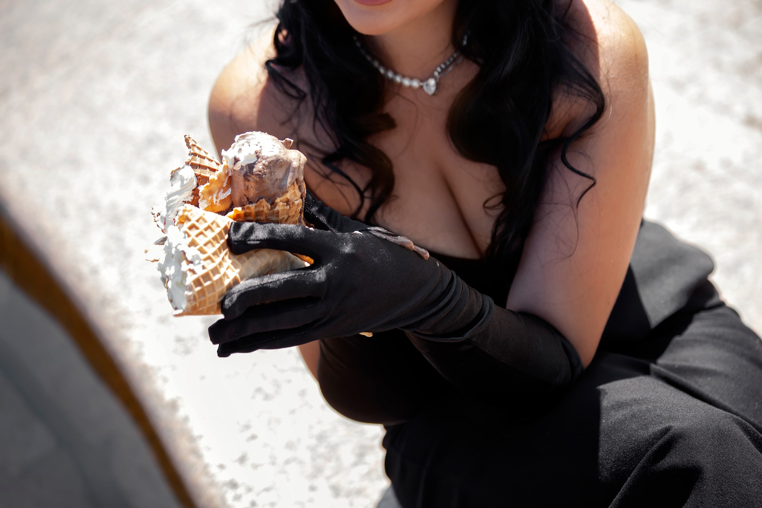 Девушка держит тающее мороженое руками в черных перчатках