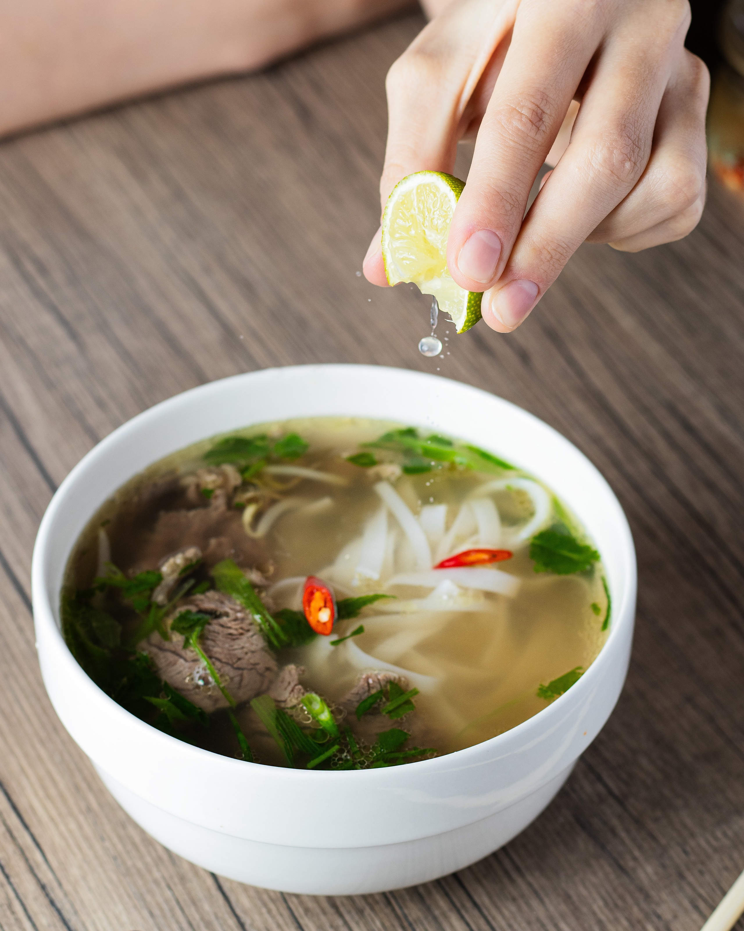 Девушка на фото выжимает лайм во вьетнамский суп фо бо