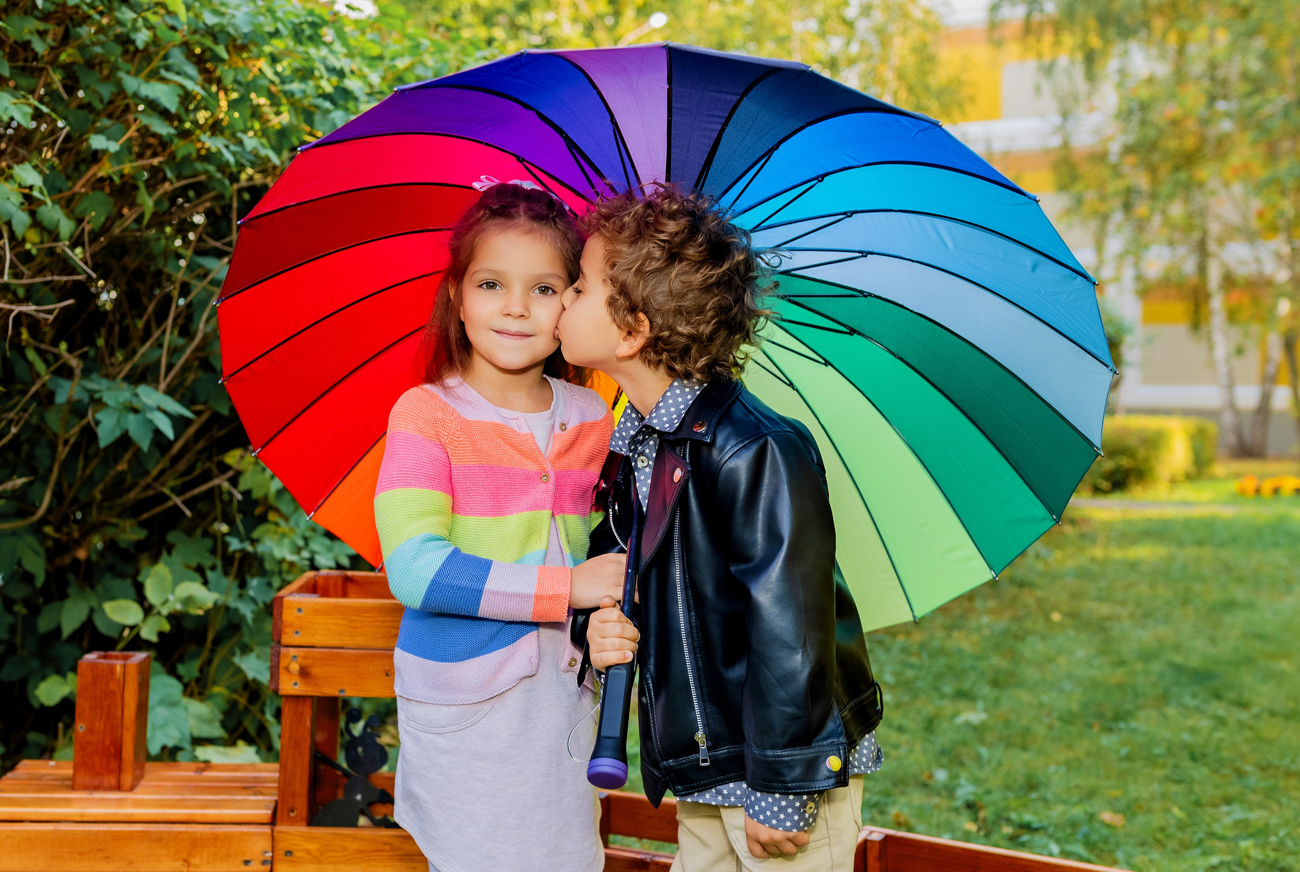 мальчик целует девочку под разноцветным зонтом